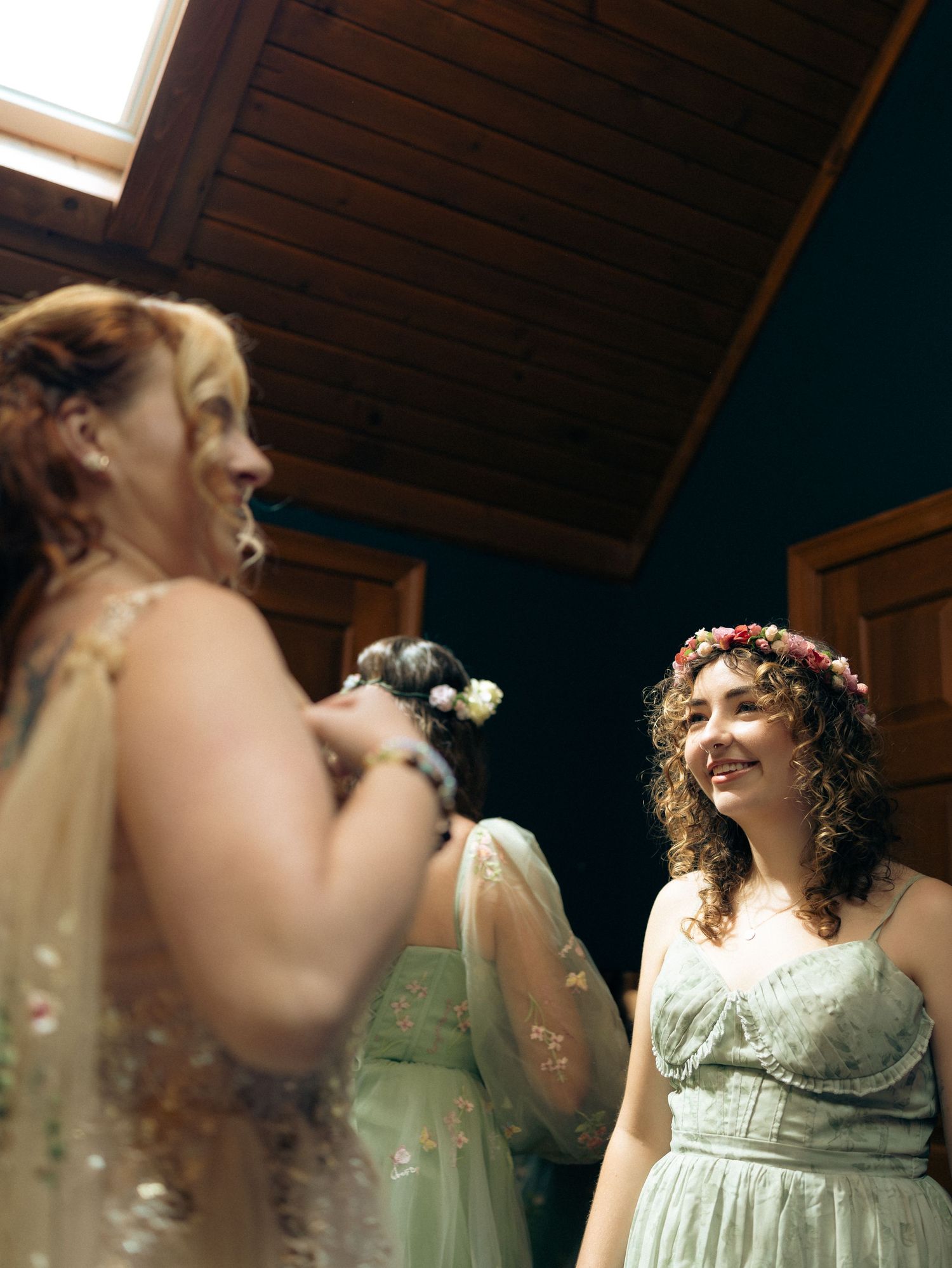 Bridesmaids in mint green dresses prepare for a wedding celebration in a rustic wooden room.