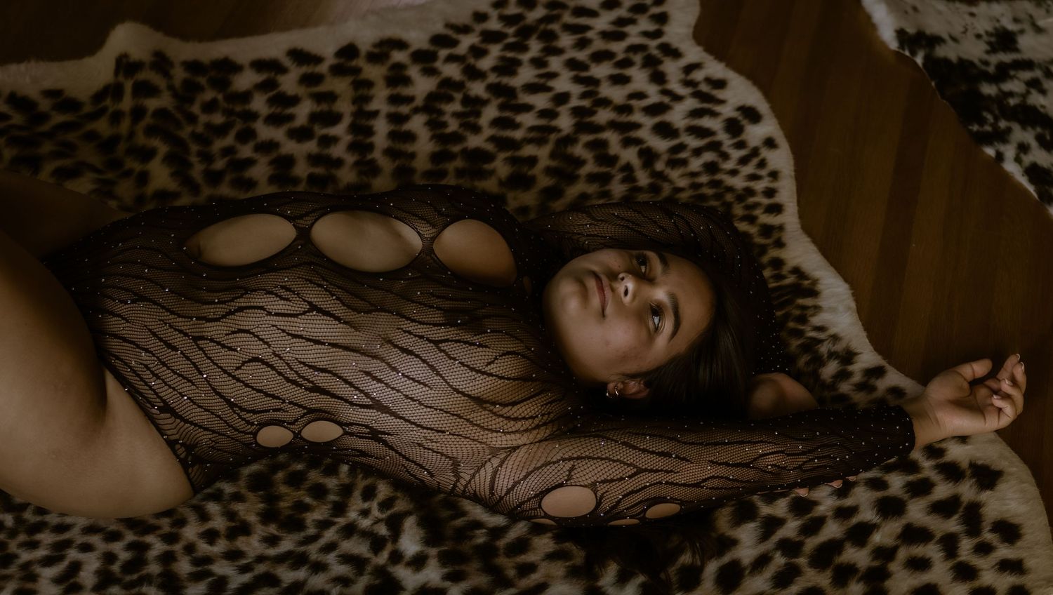 A person lounges on a leopard print blanket while wearing a sheer patterned bodysuit.