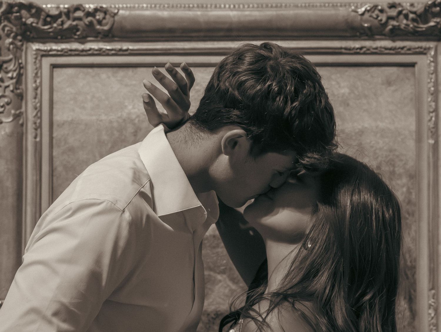 A romantic sepia-toned photograph shows a tender kiss between two people in front of an ornate picture frame.
