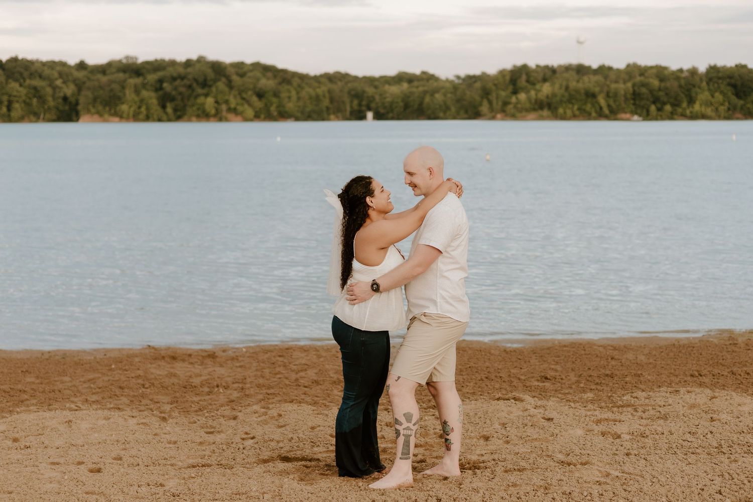 A couple shares a romantic moment on a sandy beach at sunset with the ocean in the background.