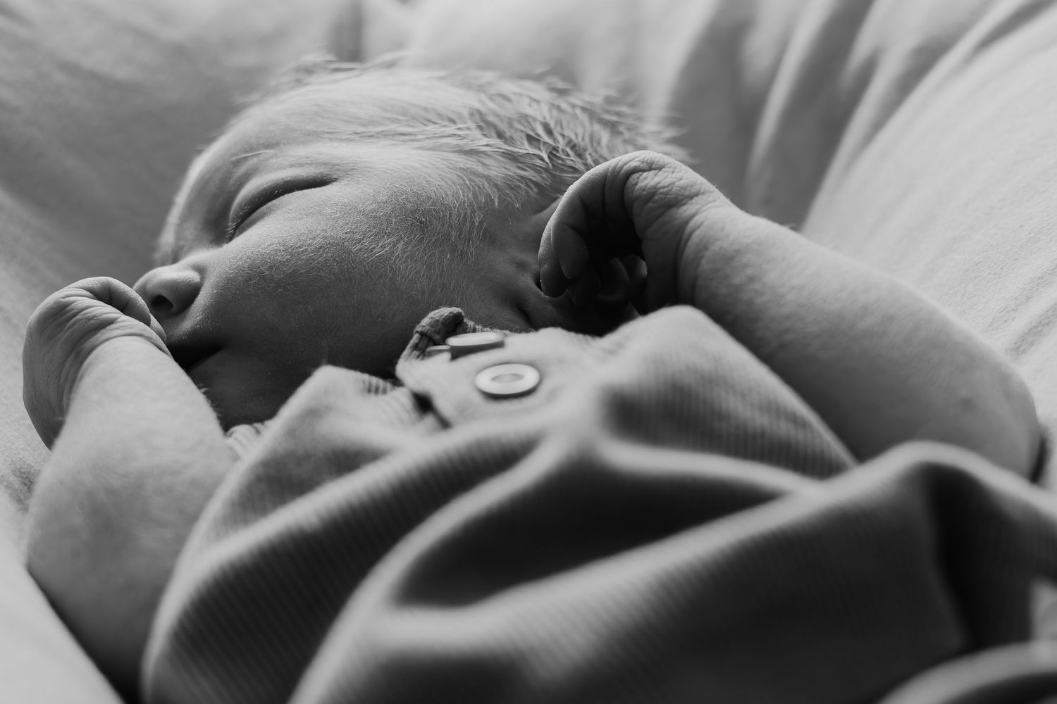 A black and white close-up photograph shows a person gently holding a sleeping newborn baby's tiny hand.