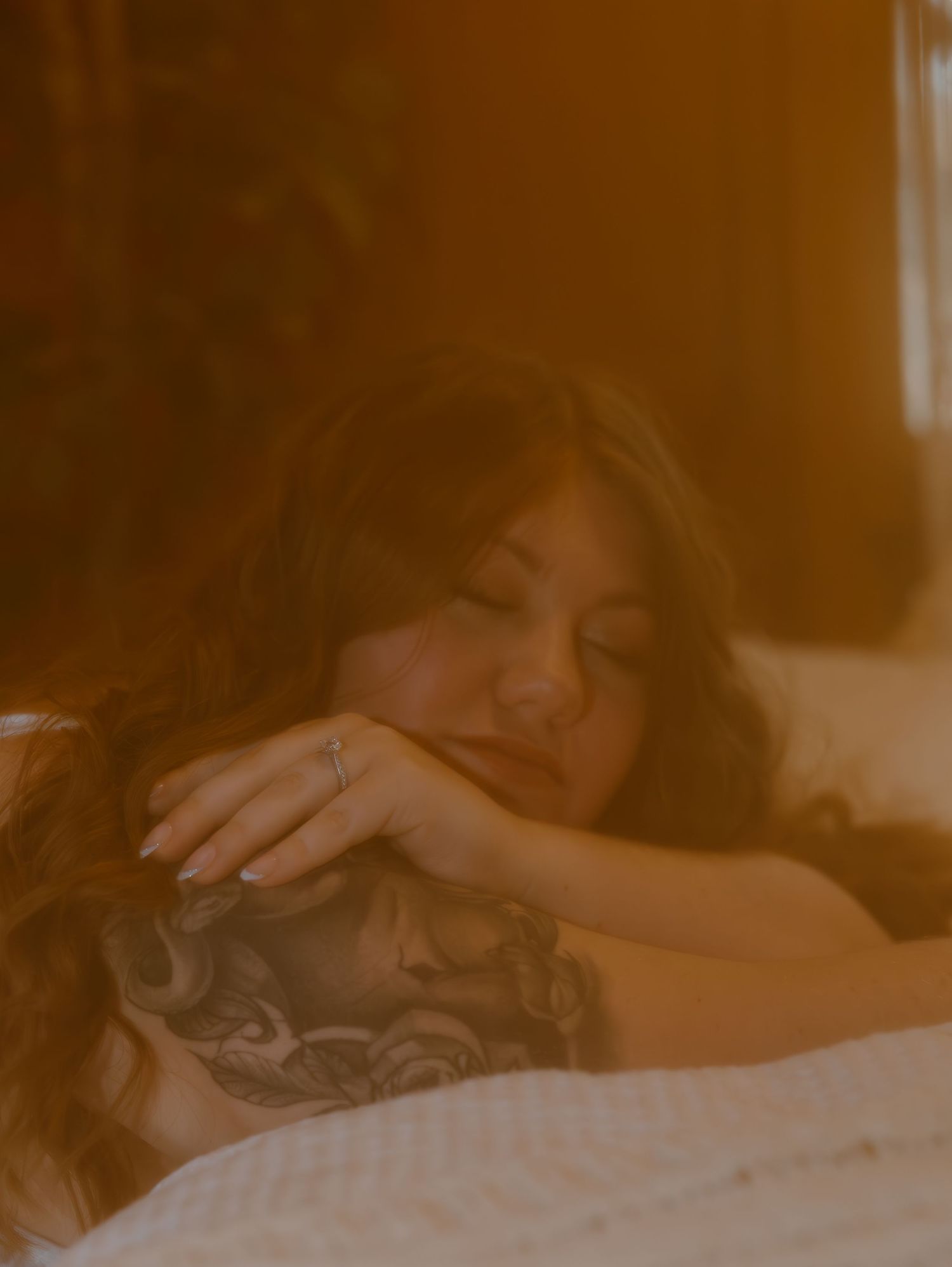 A person with dark hair rests peacefully in bed, bathed in warm sepia-toned lighting.