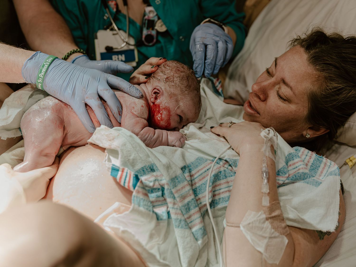 A newborn baby being placed on mother's chest immediately after birth in hospital delivery room.