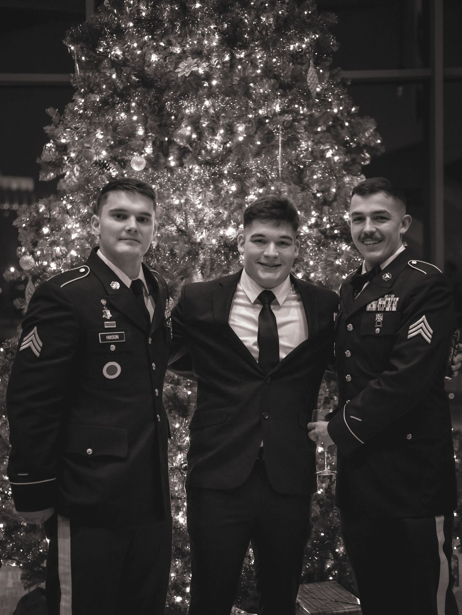 Three men in military and formal attire pose in front of a lit Christmas tree.