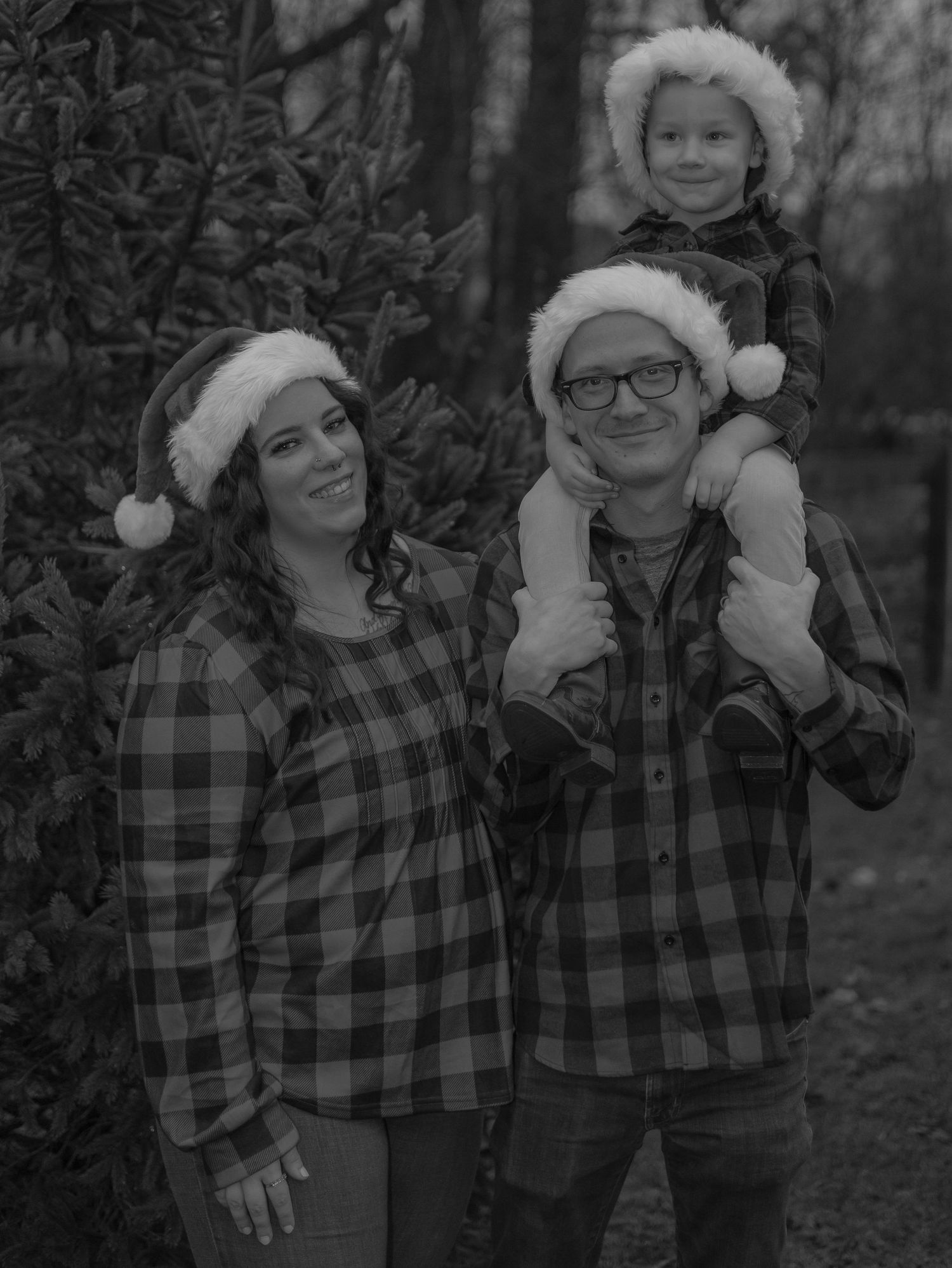 A winter family portrait with matching plaid shirts and Santa hats in black and white.