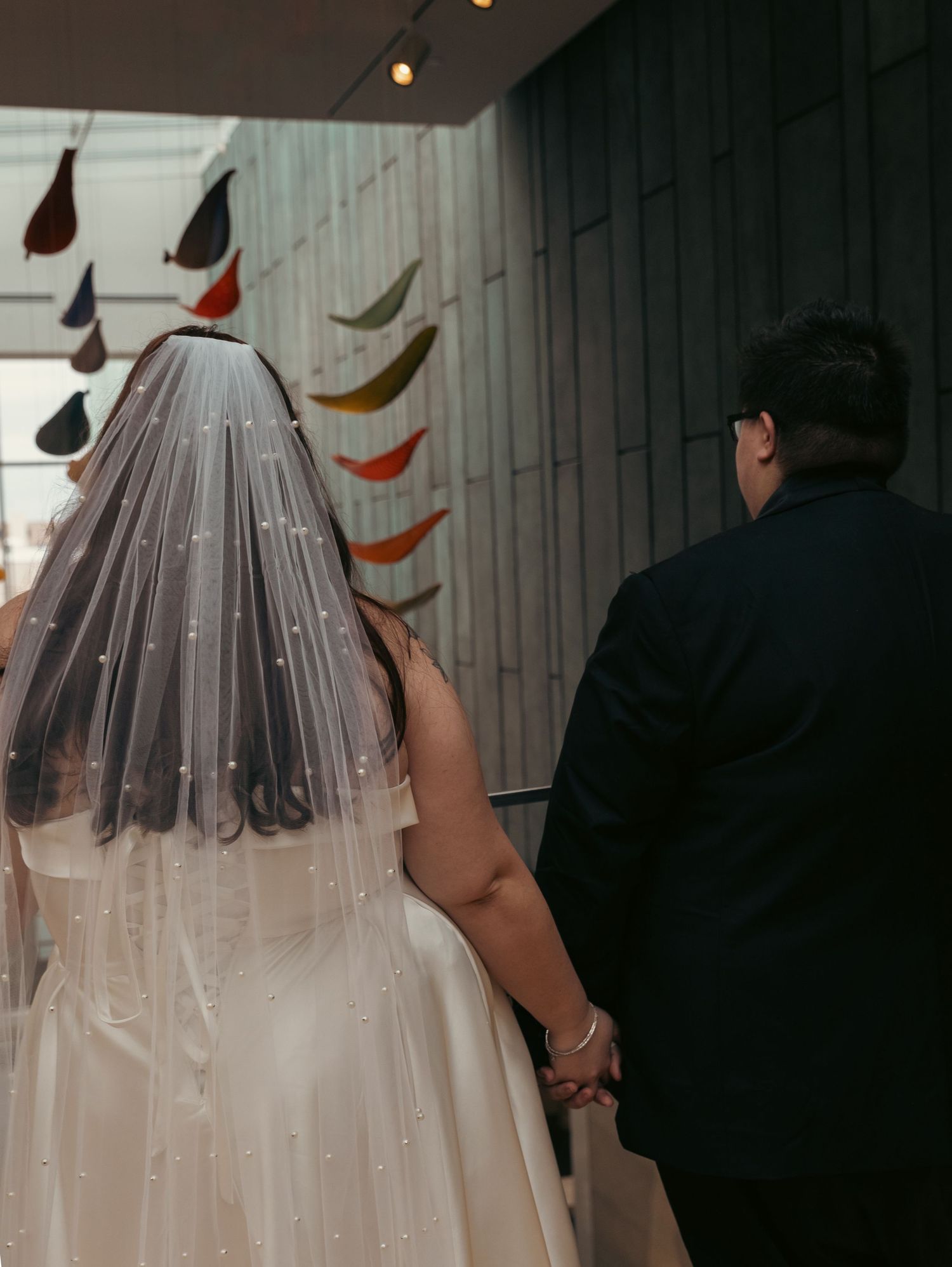 Sheer wedding veil flowing behind couple with colorful flags in background.