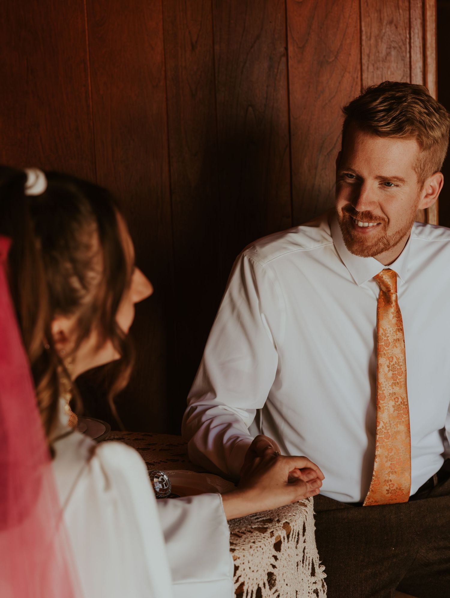 A romantic wedding couple share intimate moments in a dim room with moody lighting and a warm atmosphere.