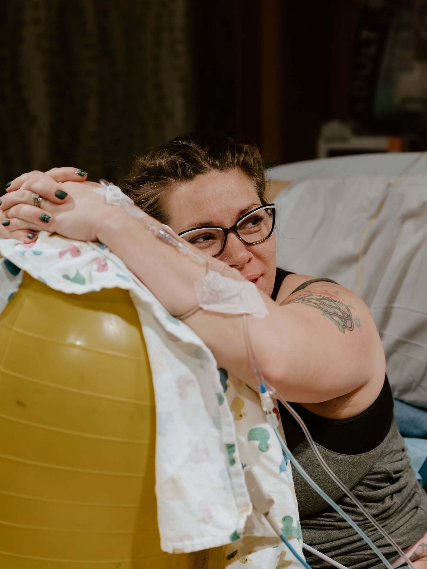 An expectant parent rests on a yellow birthing ball during labor preparation in a dimly lit room.