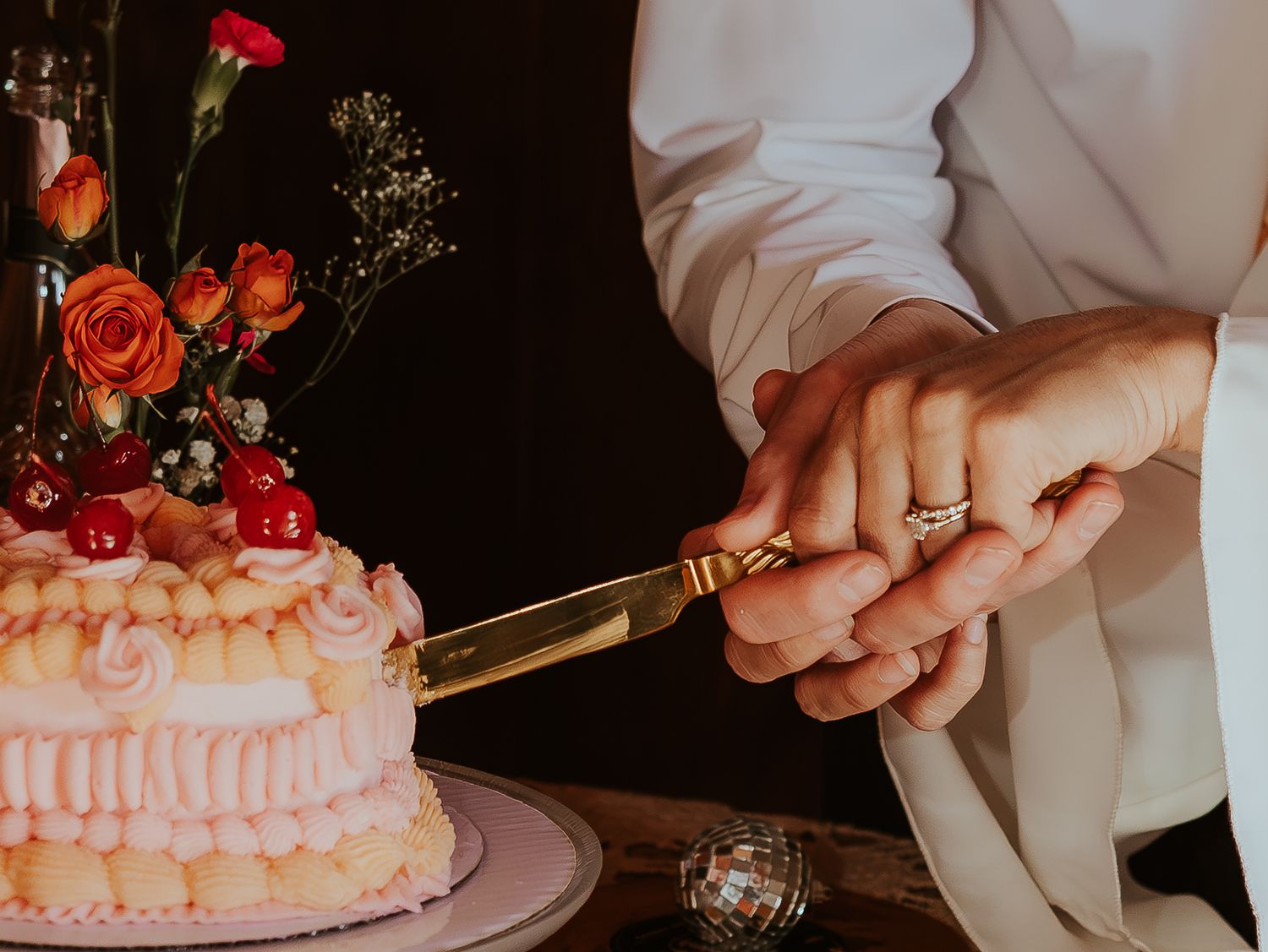 Pink frosted cake being decorated with fresh red strawberries and cherries on a dark background.