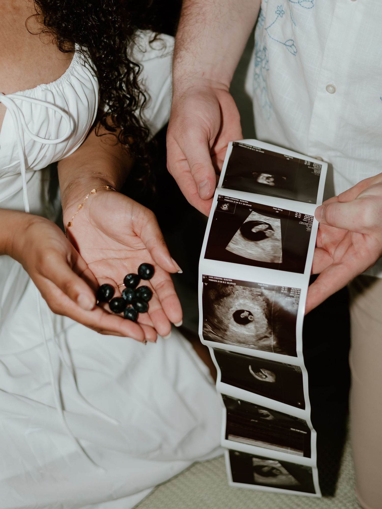 Hands holding ultrasound photos and blueberries in a pregnancy announcement photoshoot.