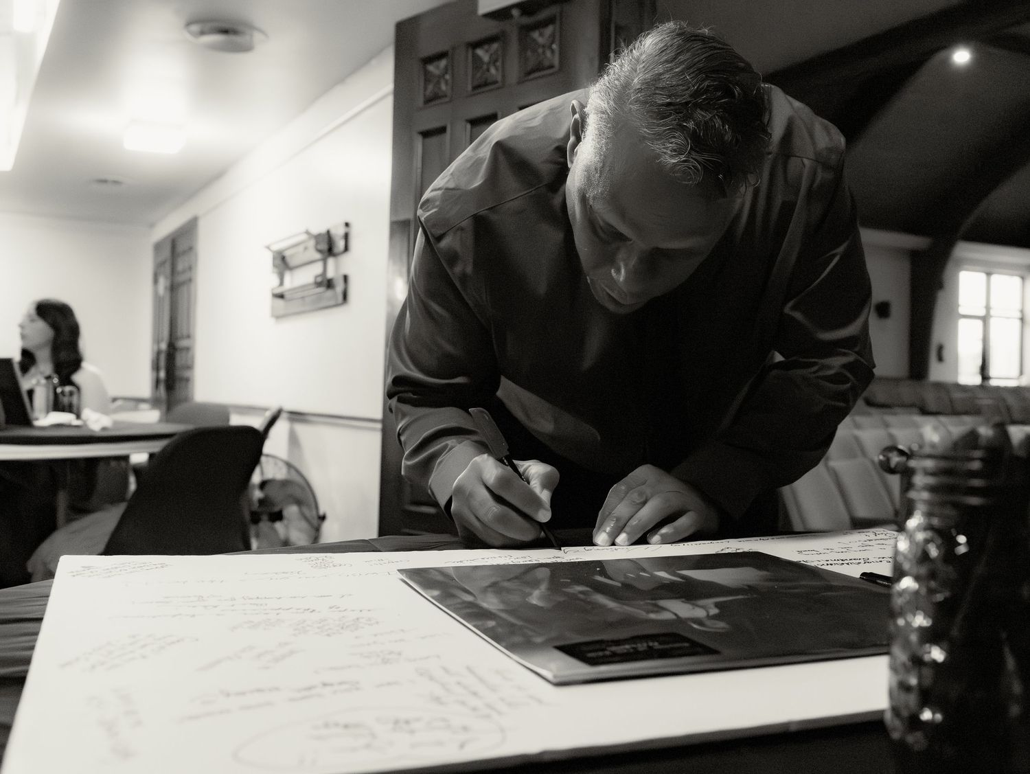 Black and white photo of wedding guest signing guestbook at reception venue table.