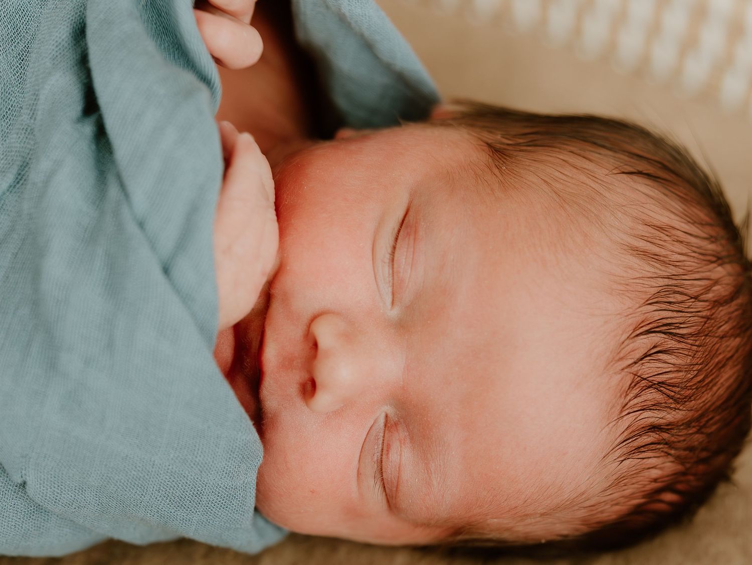 Sleeping baby wearing light colored clothing rests peacefully against turquoise bedding.