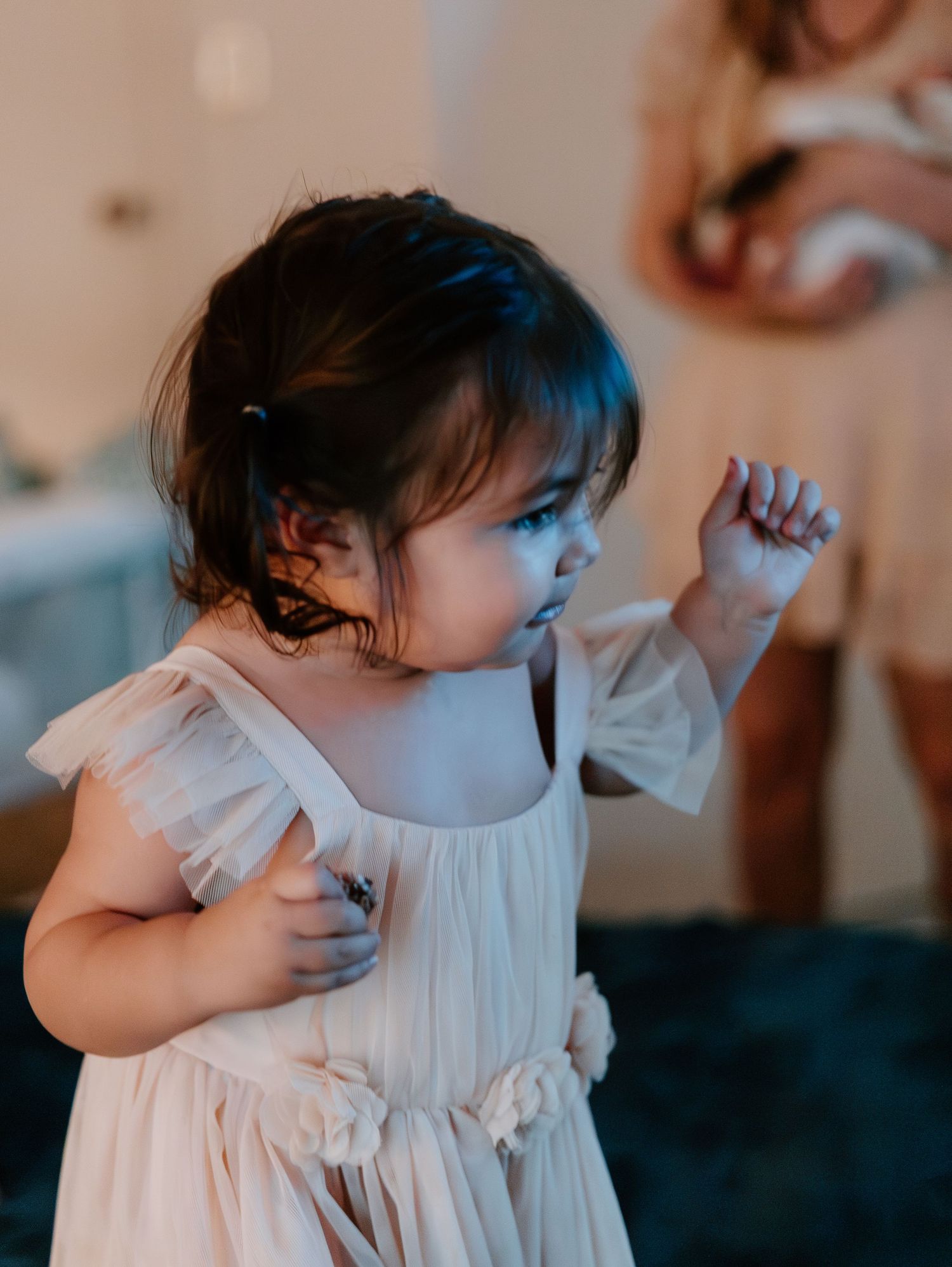 Small child in flowy white dress dancing with soft blue lighting in a candid moment.