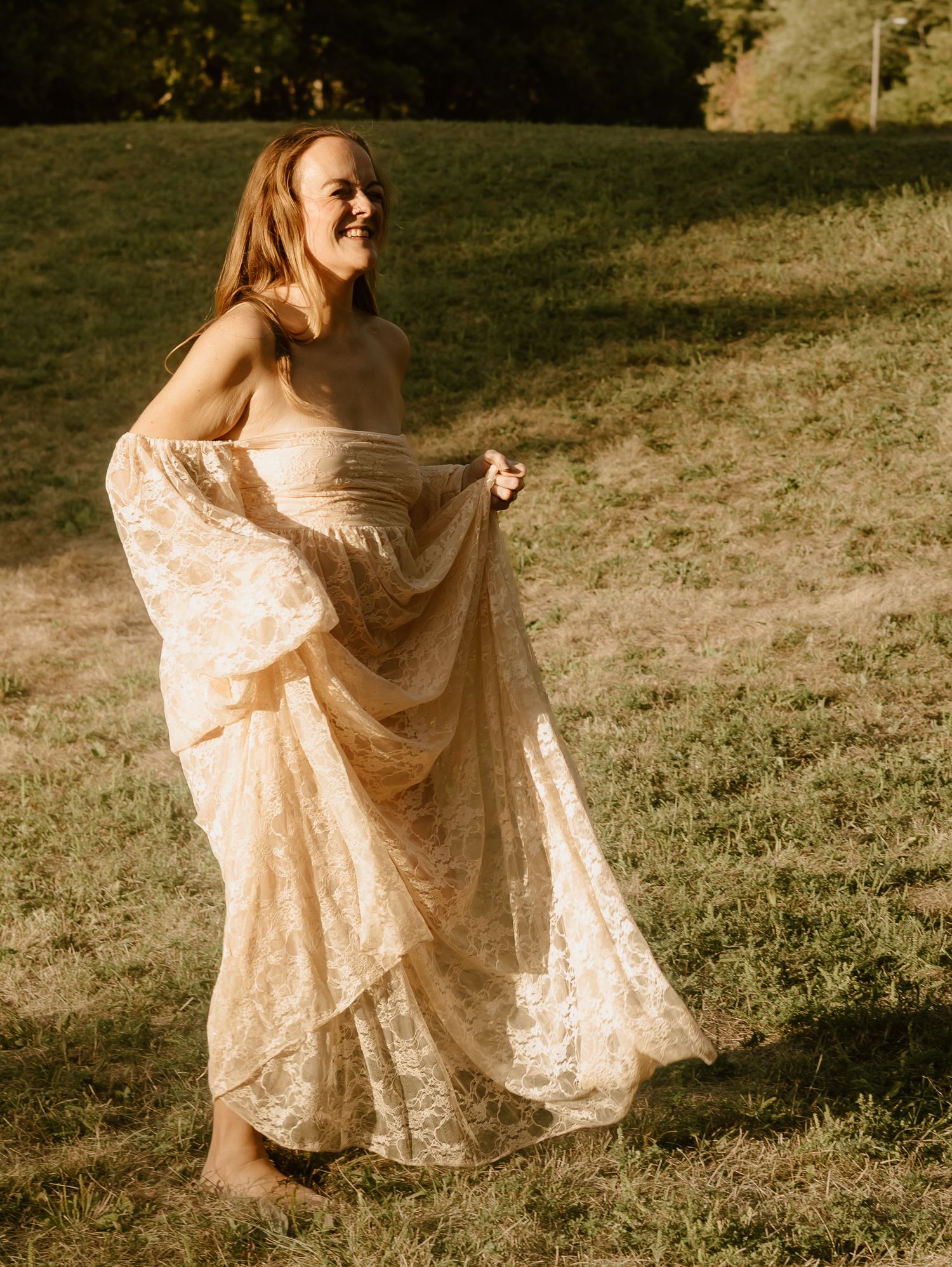 A person in a flowing cream lace dress twirls gracefully in a sunlit meadow during golden hour.