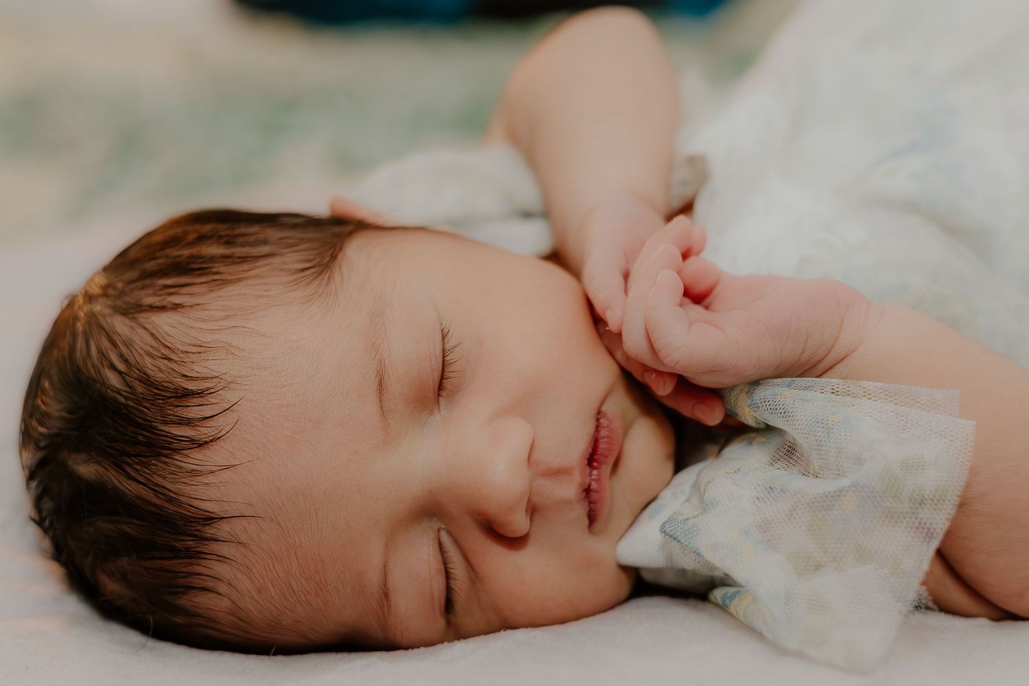 Sleeping baby in white onesie rests peacefully on soft white bedding.