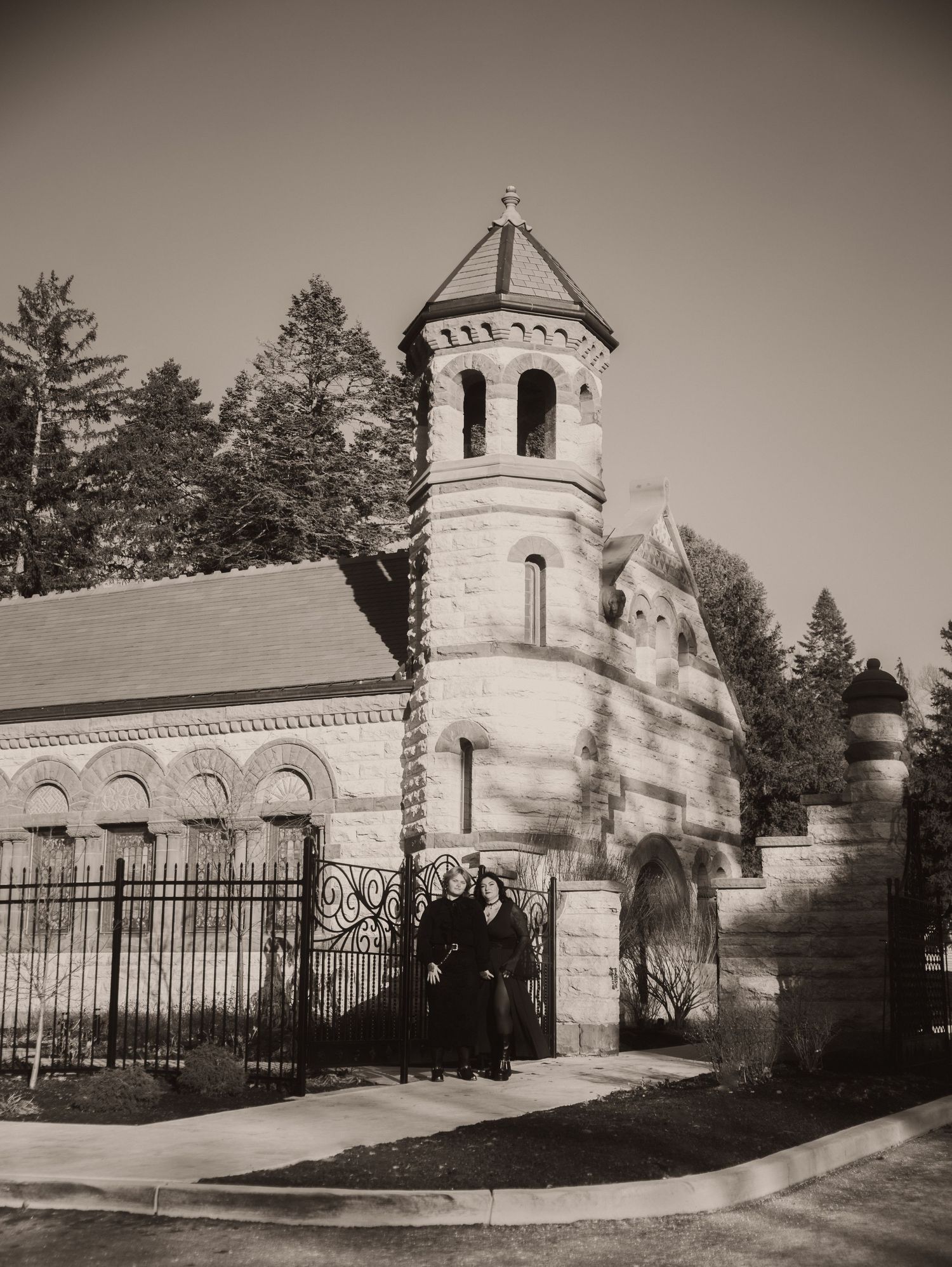 Historic cemetery entrance with white stone chapel and ornate iron gates in sepia tones.