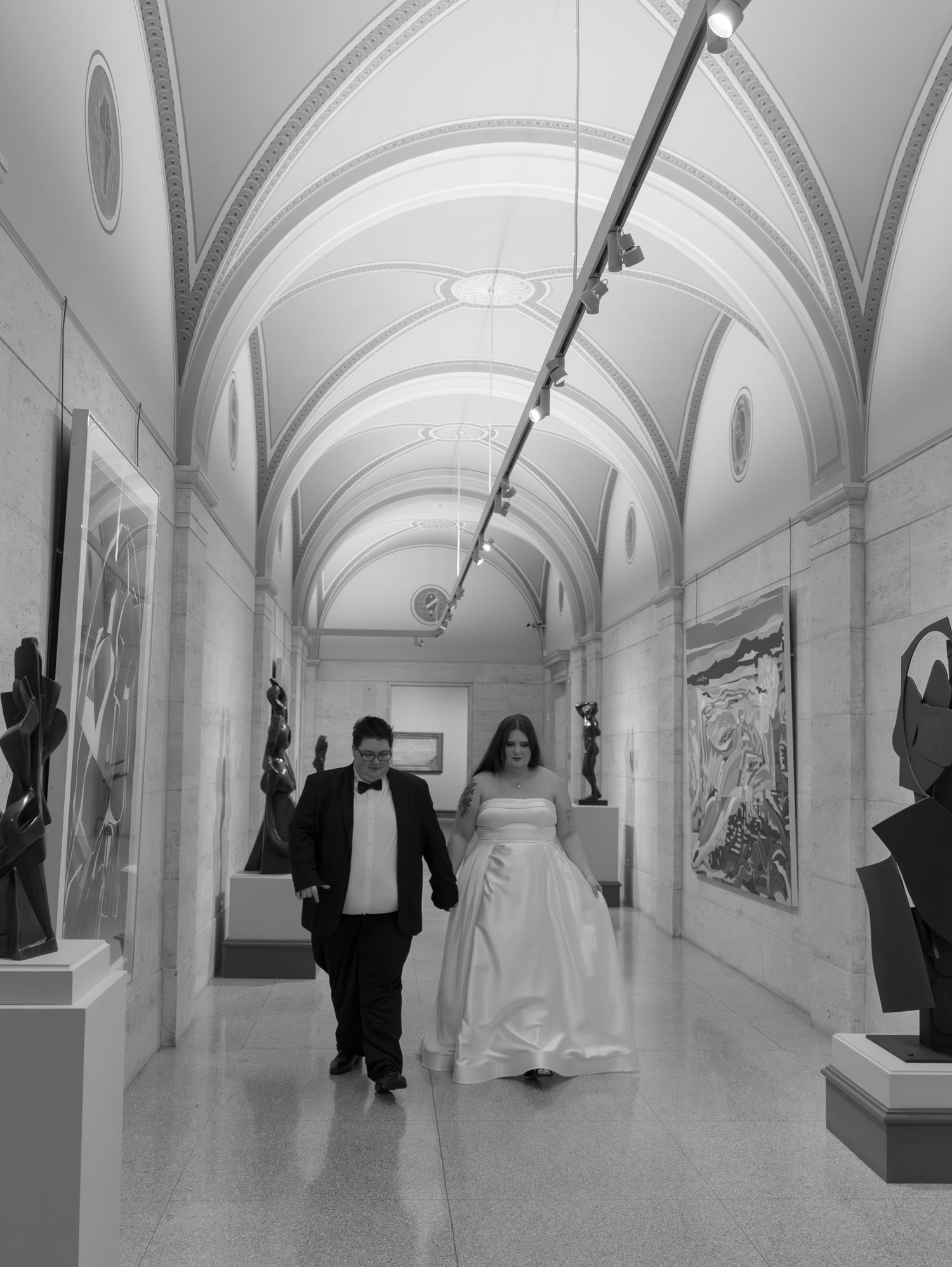 An elegant arched gallery hallway with white walls displays artwork and sculptures under vaulted ceilings.