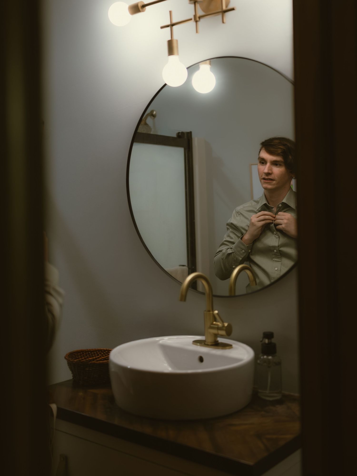 Modern bathroom interior with round mirror, pendant lights, and wooden vanity creating a moody atmosphere.