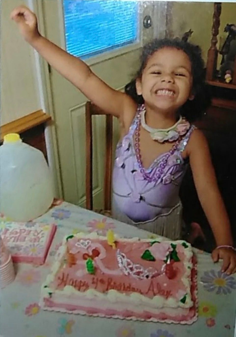 A child celebrating at a birthday party with a pink decorated cake and balloons.