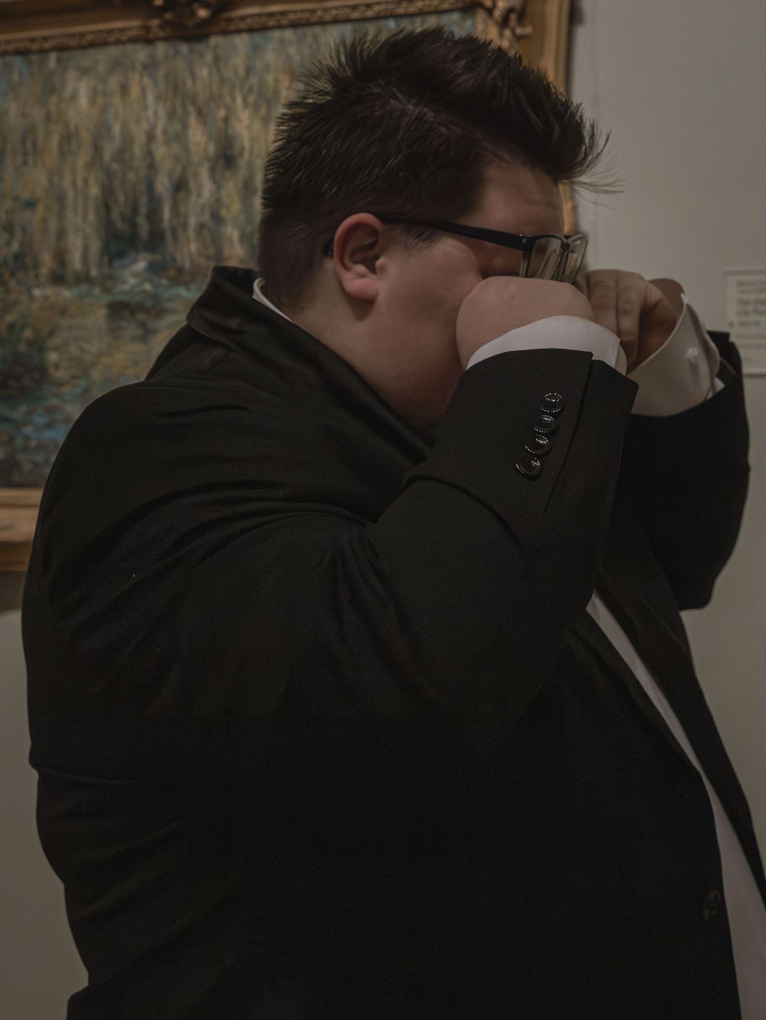 Person in dark clothing leans against a wall in dim lighting.