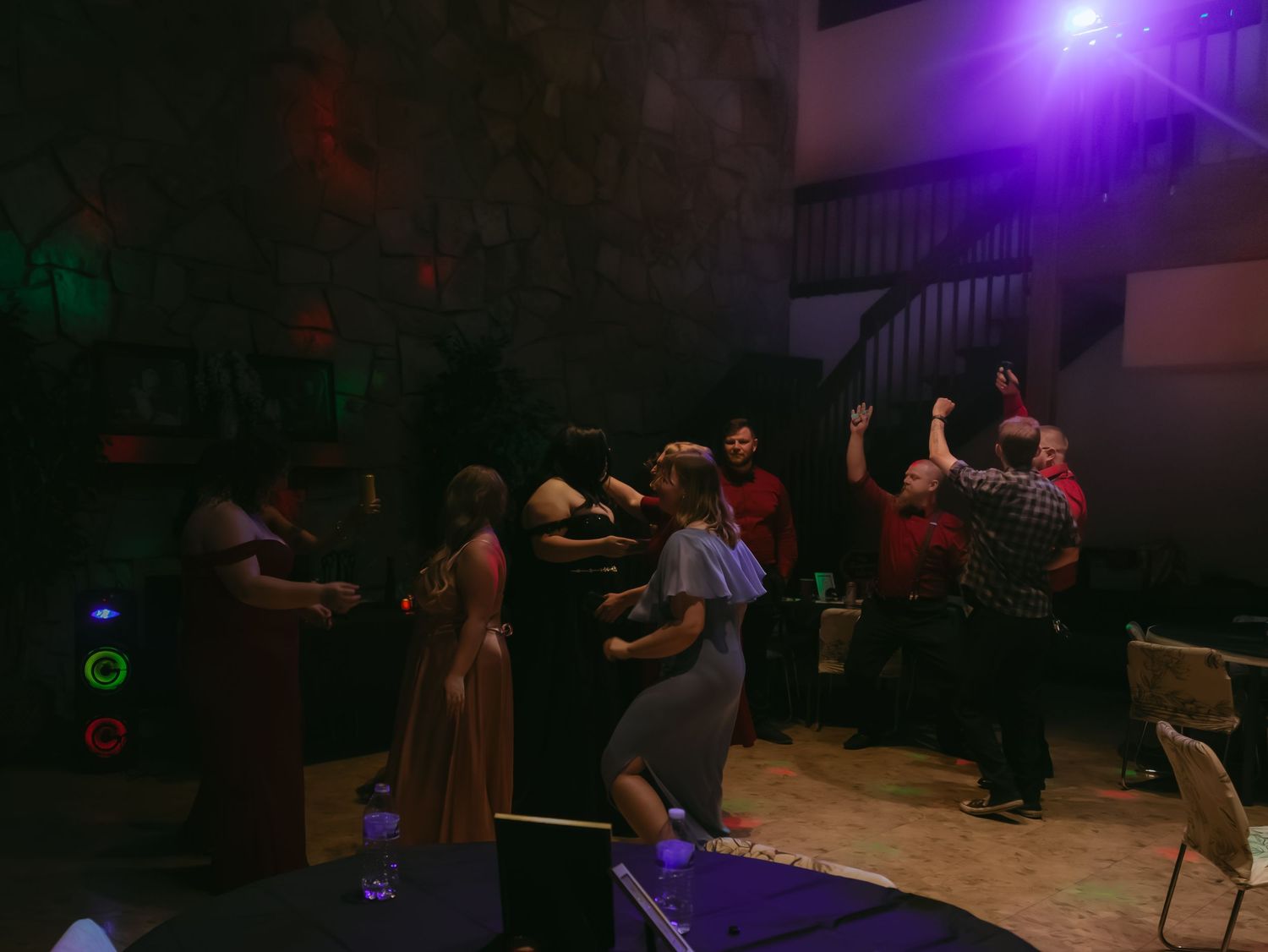 Group of people dancing and celebrating at an indoor party with colorful purple and green DJ lights.