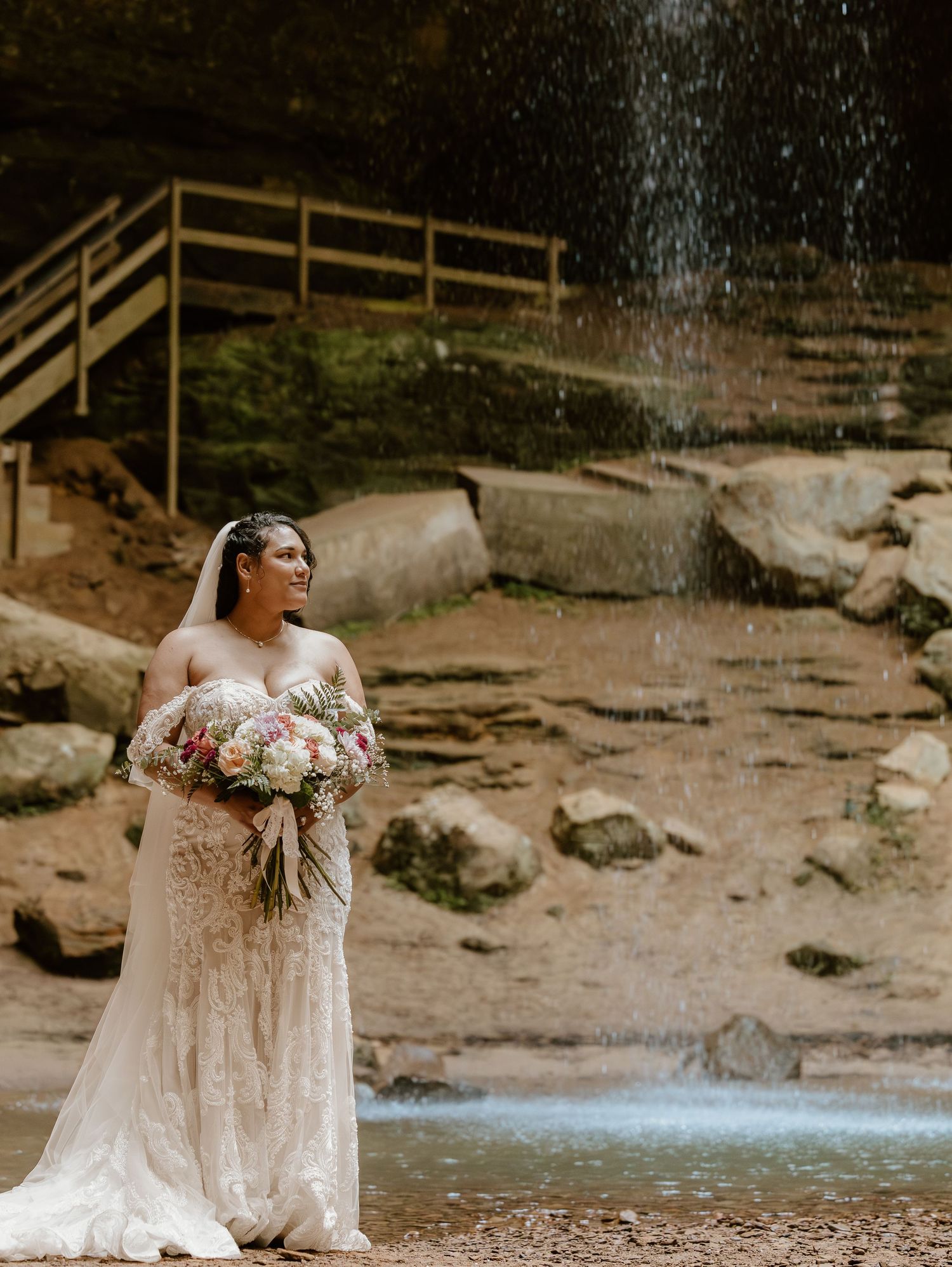 Wedding photography scene at a waterfall with a bride holding a pink and white bouquet.