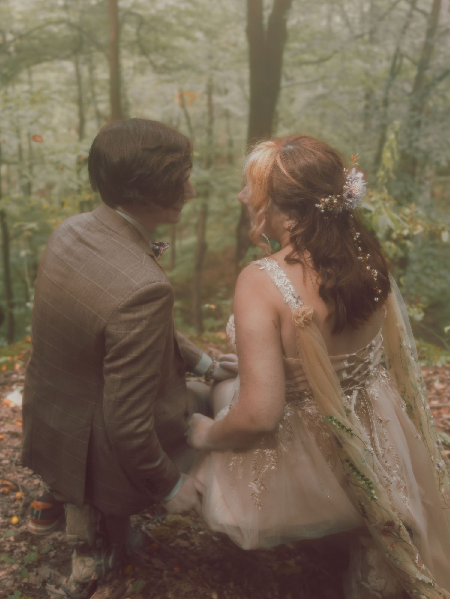 Back view of couple in champagne dress and brown suit during forest wedding ceremony.