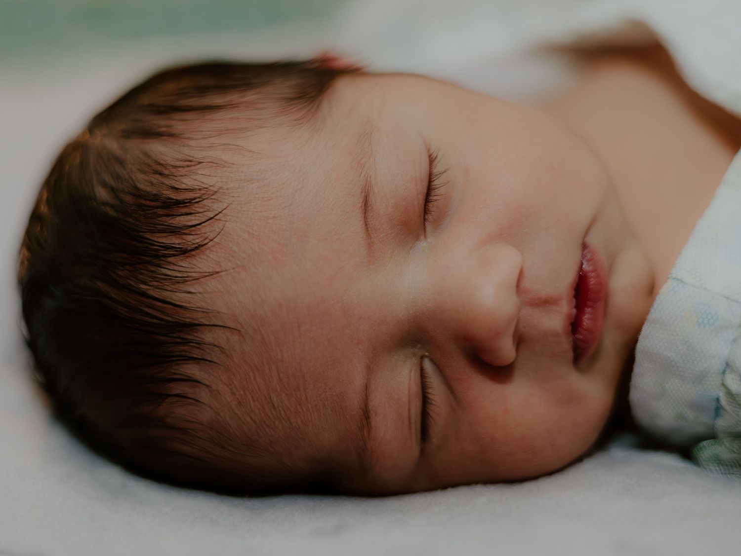A peaceful sleeping baby rests on white bedding with soft lighting creating a calm and tranquil mood.