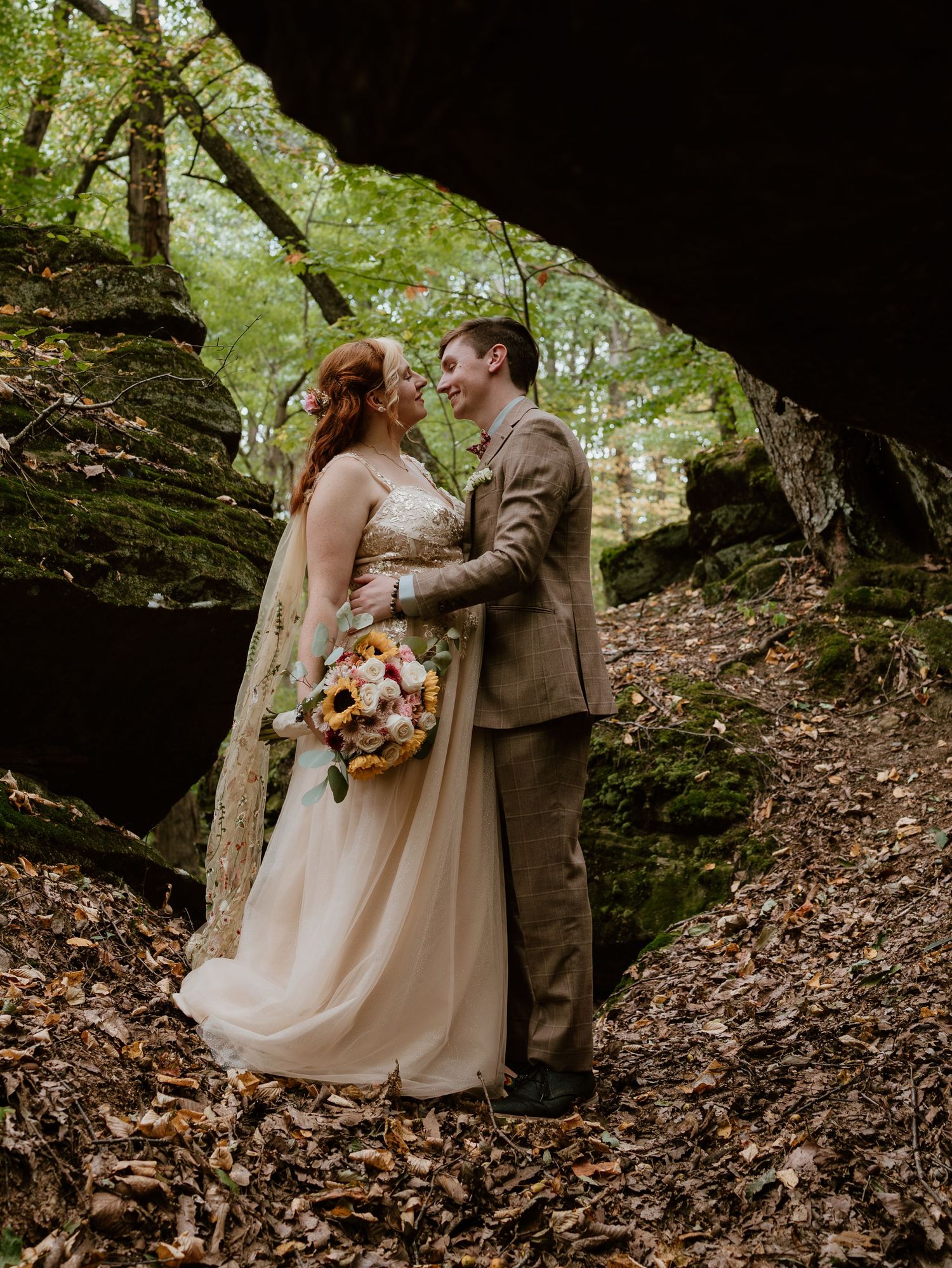 Couple in fall forest embraces intimately surrounded by autumn leaves and natural woodland scenery.