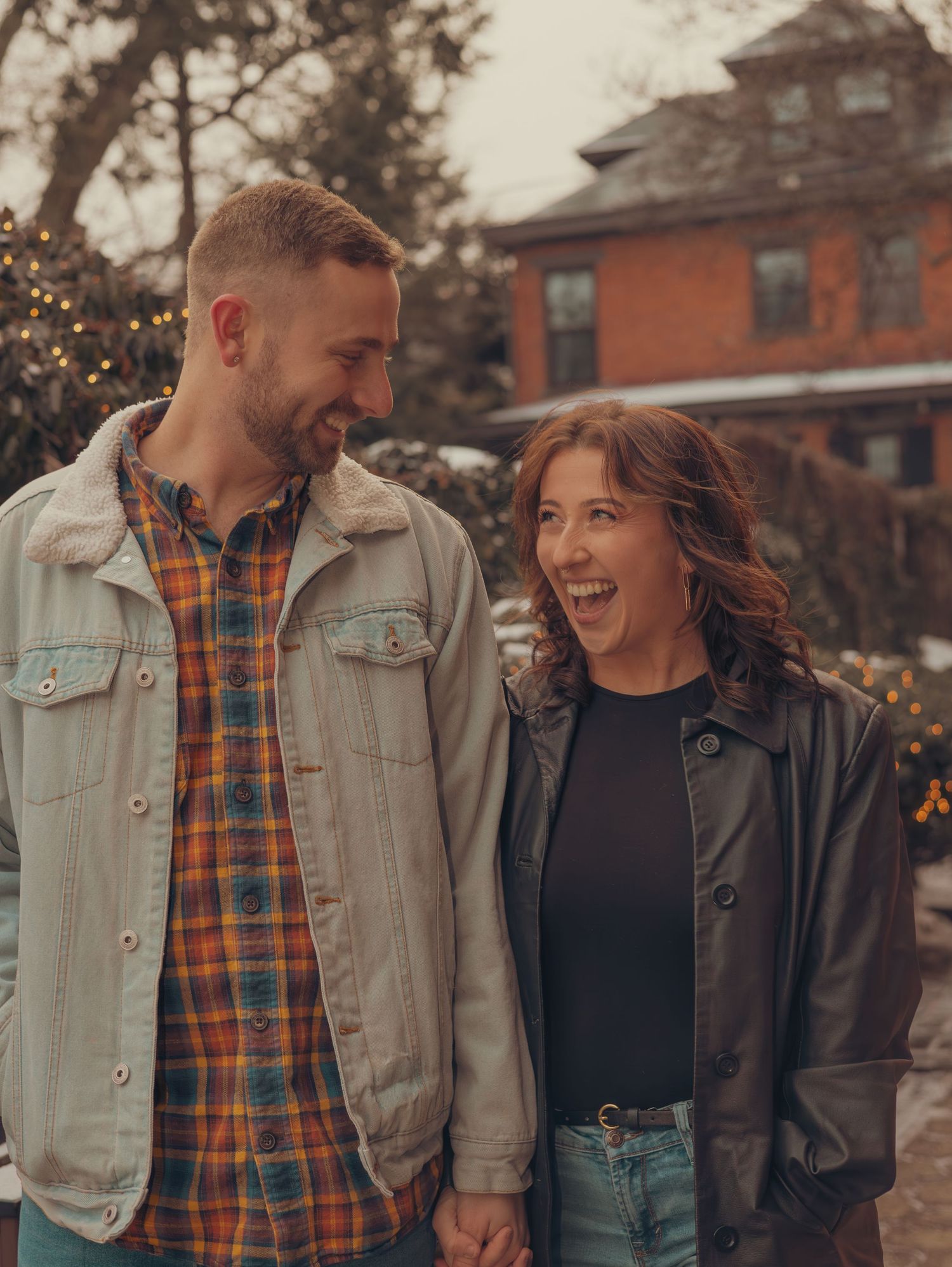 A casual couple shares a laugh while walking outdoors near brick buildings on an autumn day.