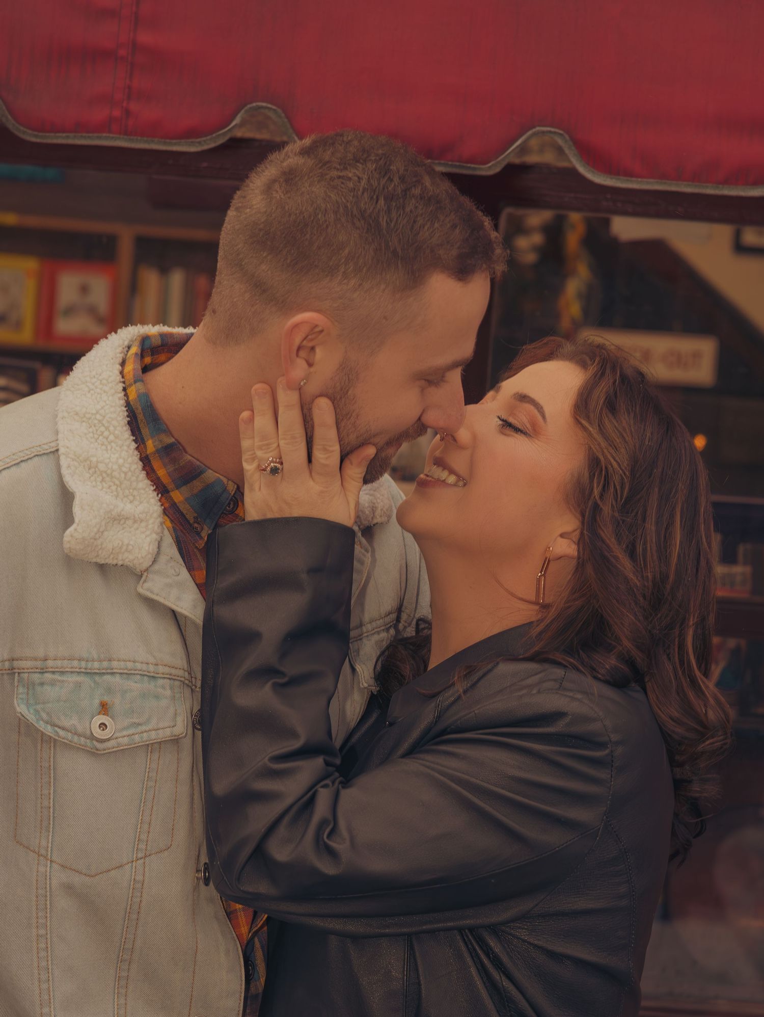 A romantic couple sharing a tender kiss while leaning against a brick wall in warm lighting.