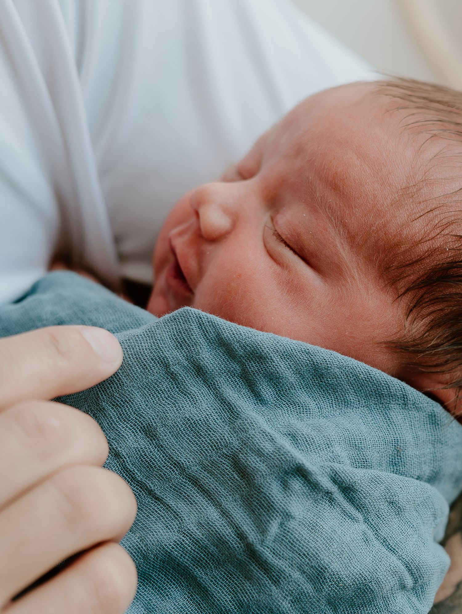 Peaceful newborn baby sleeping soundly while swaddled in a soft teal blanket.