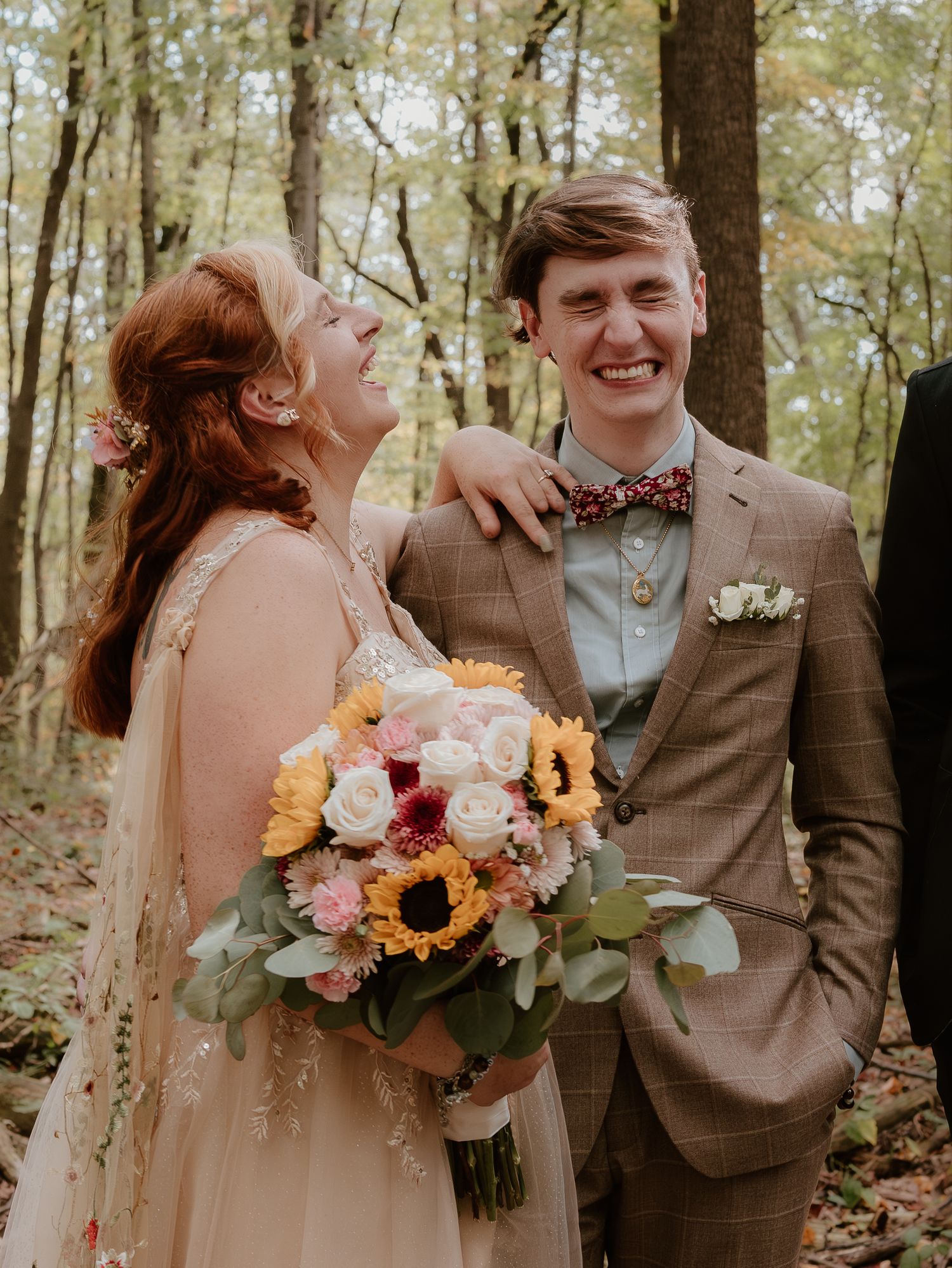 A joyful autumn wedding moment captured in the woods with sunflowers and pink florals in the bouquet.
