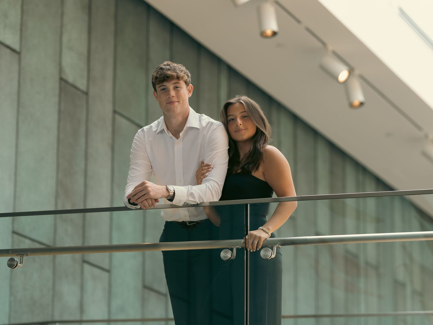 People lean over glass railings in a modern office building interior with sleek architectural design.