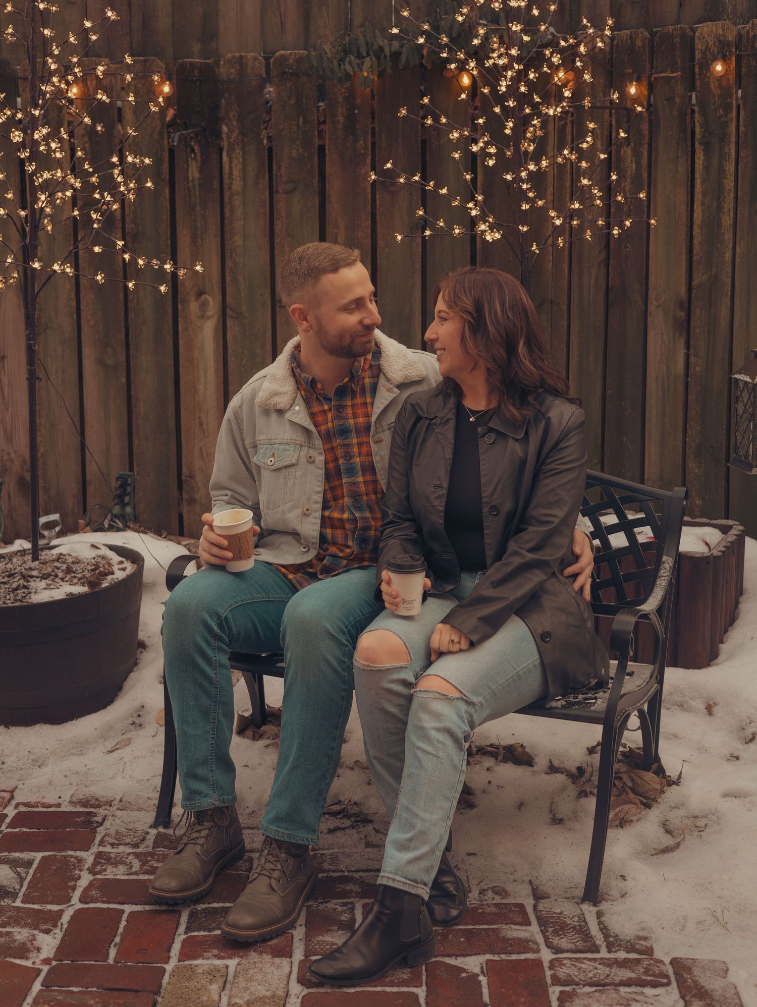 A couple sits on a bench surrounded by twinkling lights and snow in a romantic winter setting.