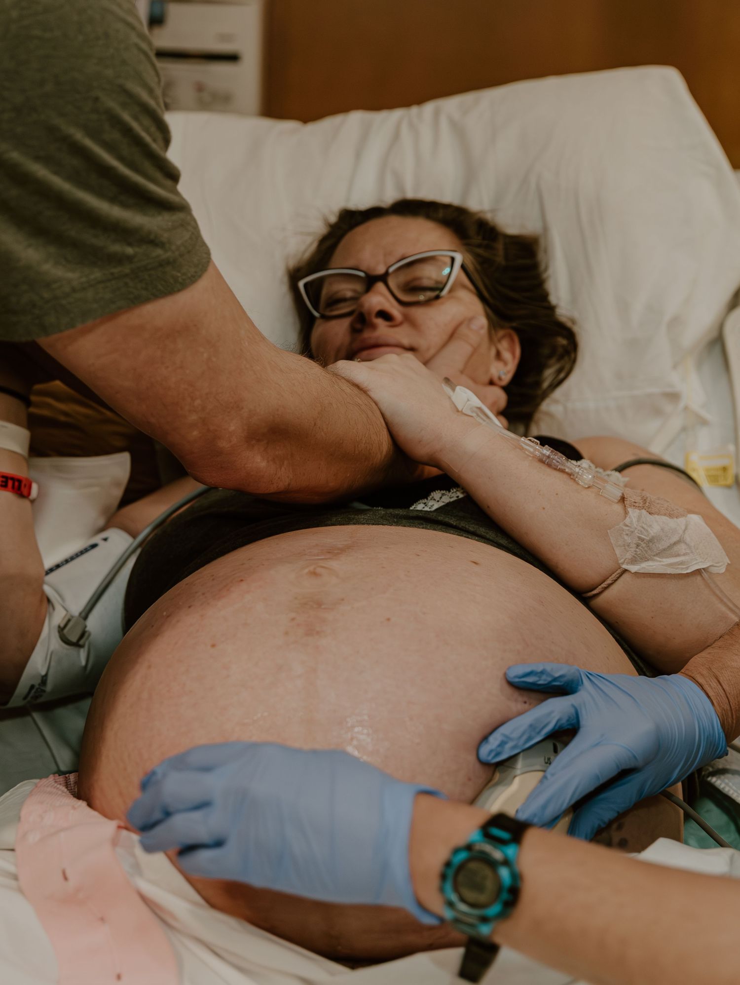 Medical professional wearing blue gloves performs an examination on a patient lying on white hospital bed.