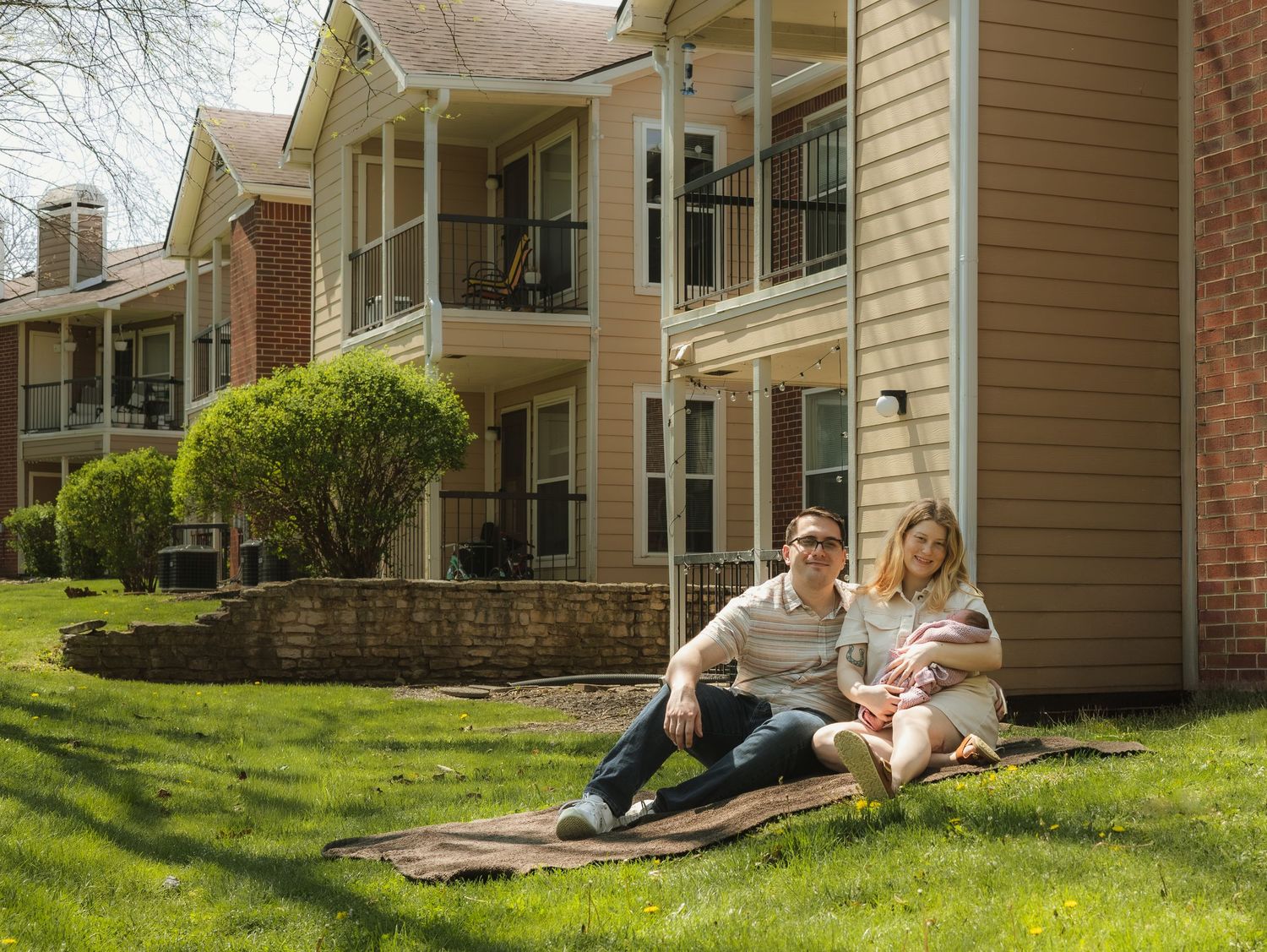 Couple relaxing on a blanket in the green lawn of a suburban apartment complex on a sunny day.