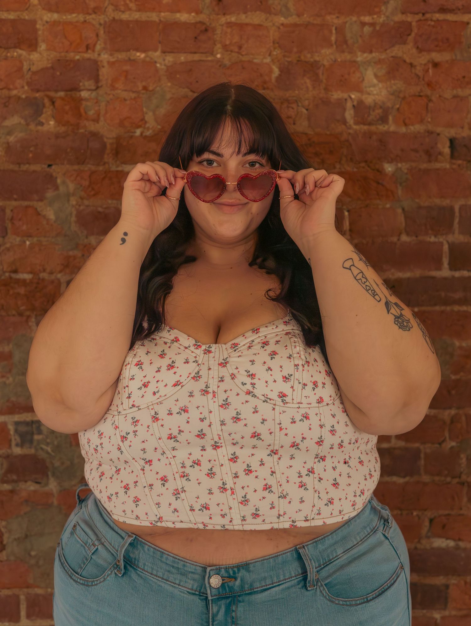 A confident pose in a floral crop top and jeans against exposed brick.