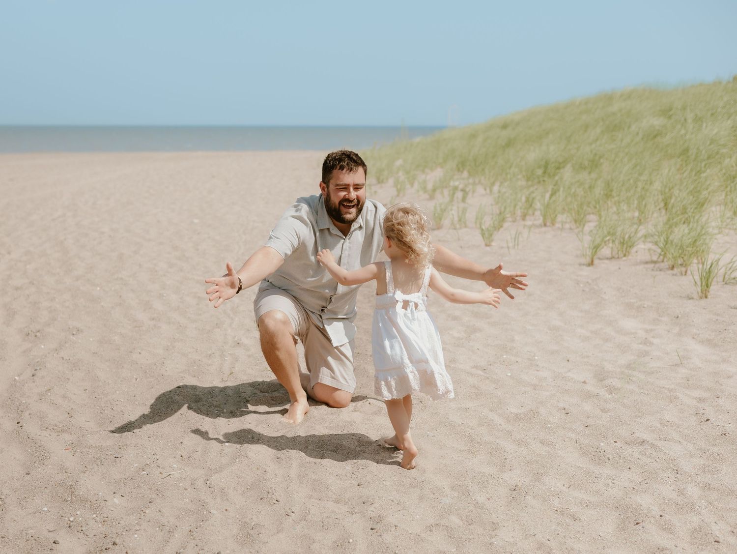 Playful sequence of someone running and jumping on a sandy beach with grassy dunes in the background.