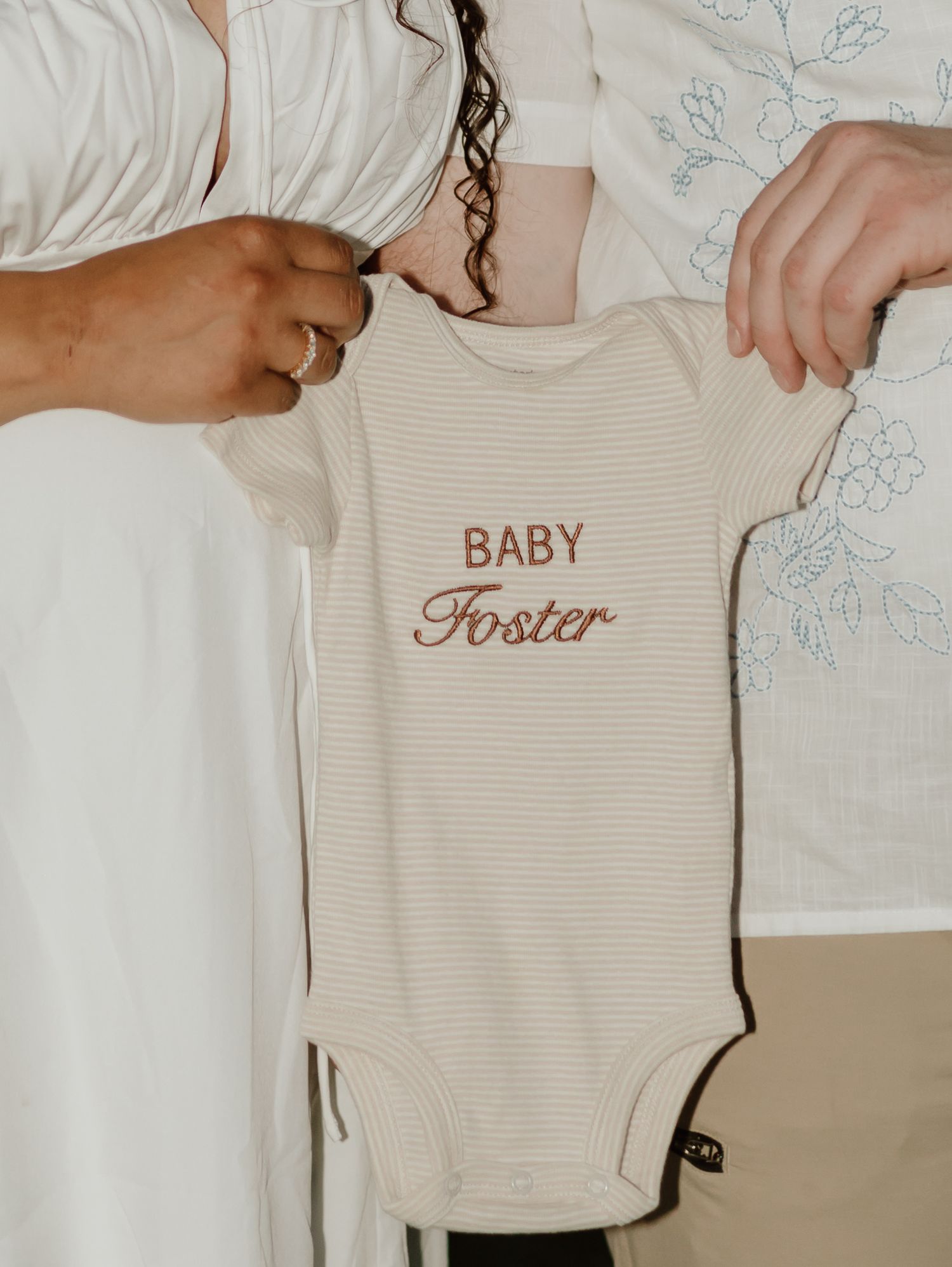 A series of neutral-colored baby onesies and clothing items laid out in a soft, minimalist style.