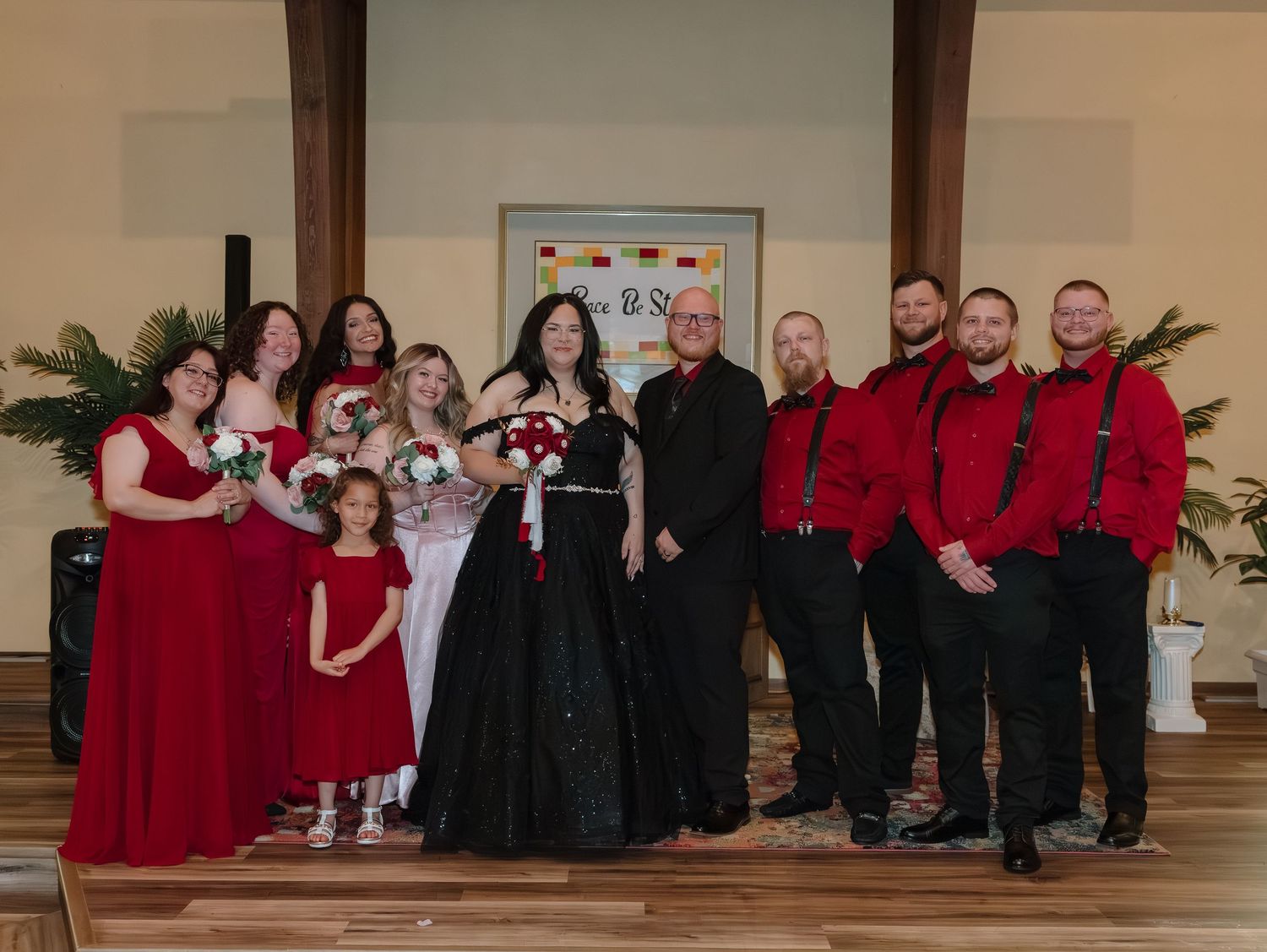 Wedding party poses in church wearing black and red attire with bride in black gothic gown.