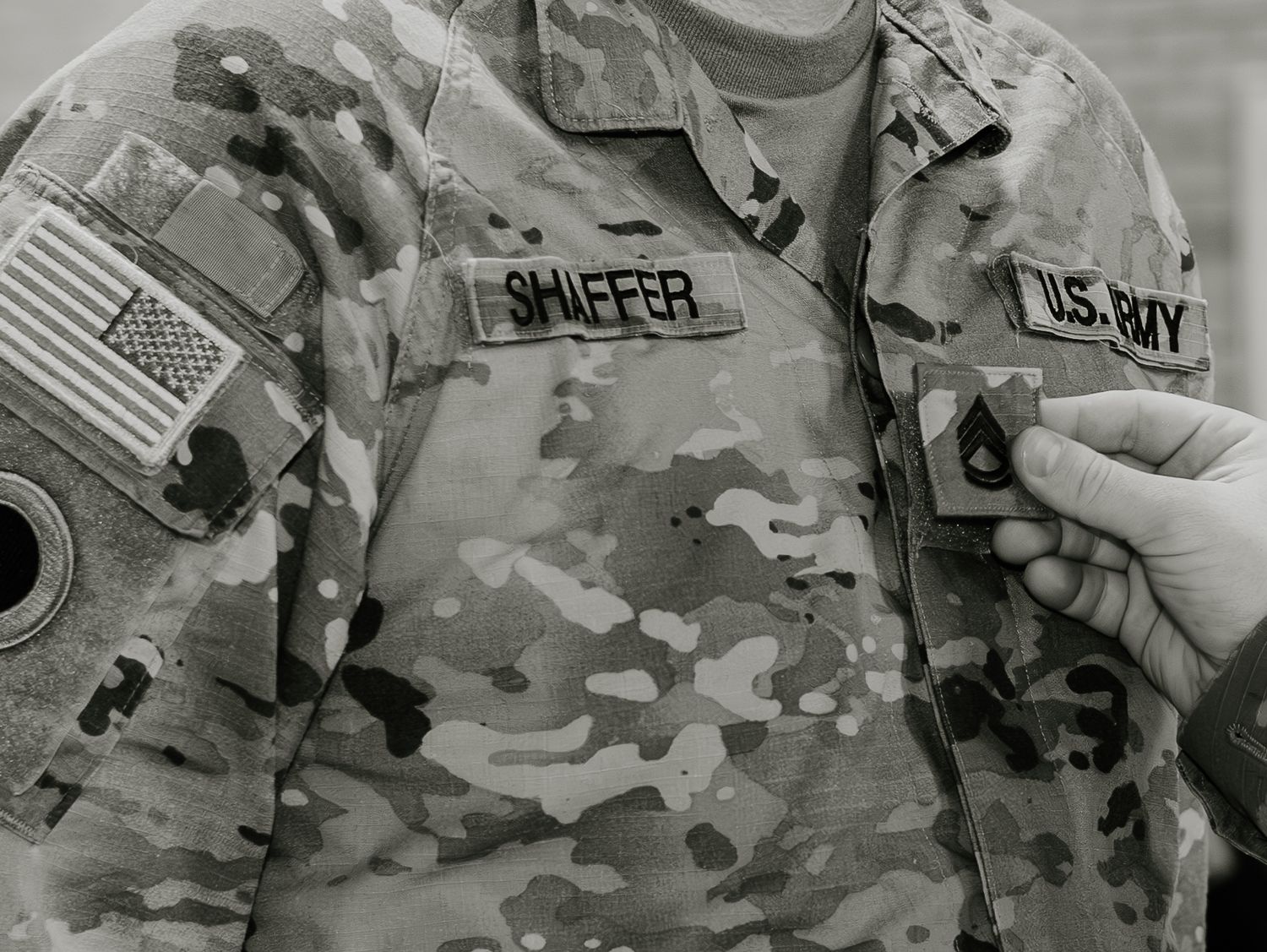 A military uniform showing U.S. Army camouflage pattern with patches and insignia on the sleeve.