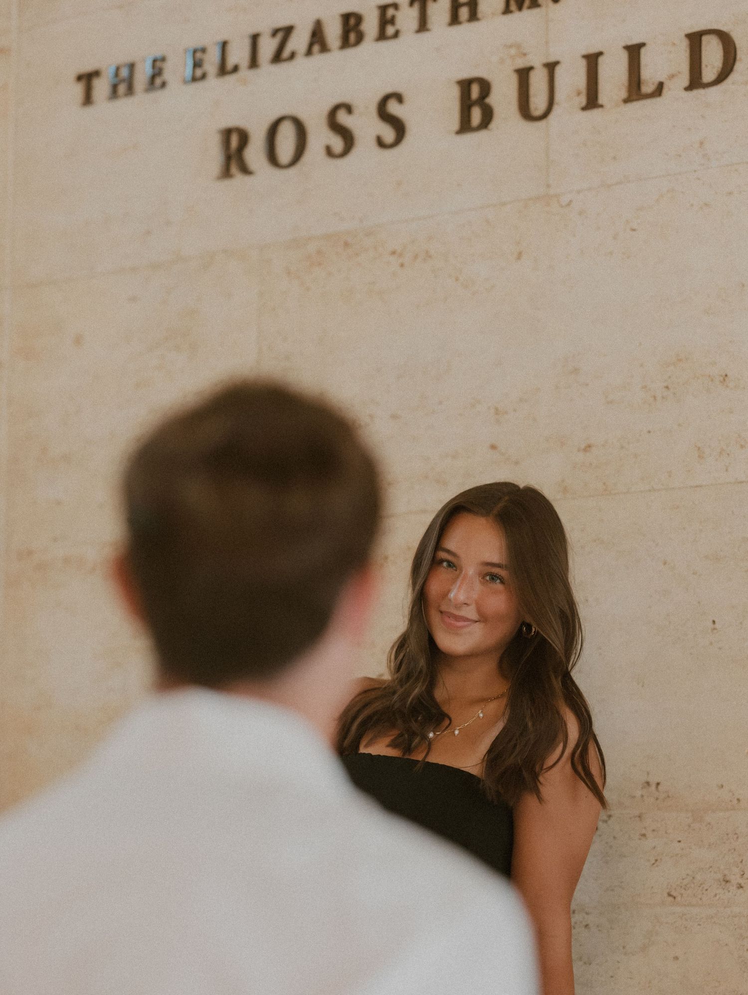 A romantic photoshoot against a stone wall with architectural text visible.