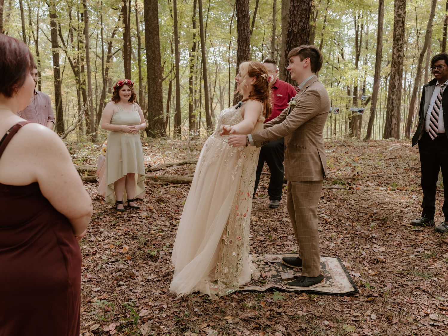 A romantic woodland wedding ceremony taking place among tall trees with guests gathered in the forest.