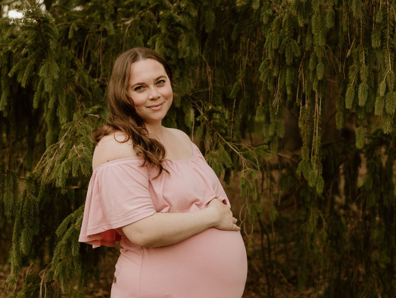 Woman wearing a pink dress poses in a garden setting against a backdrop of cascading greenery and foliage.