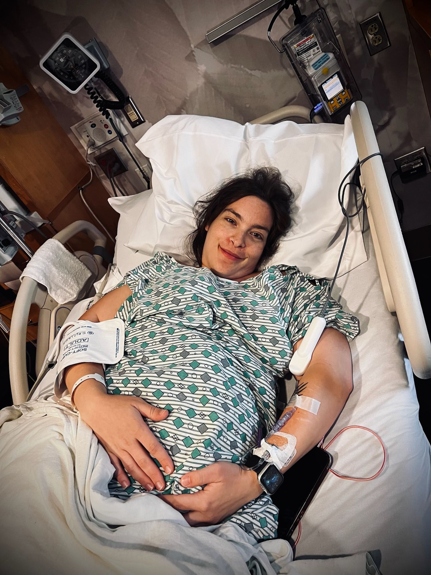 Hospital room scene with medical equipment and patient in patterned gown.
