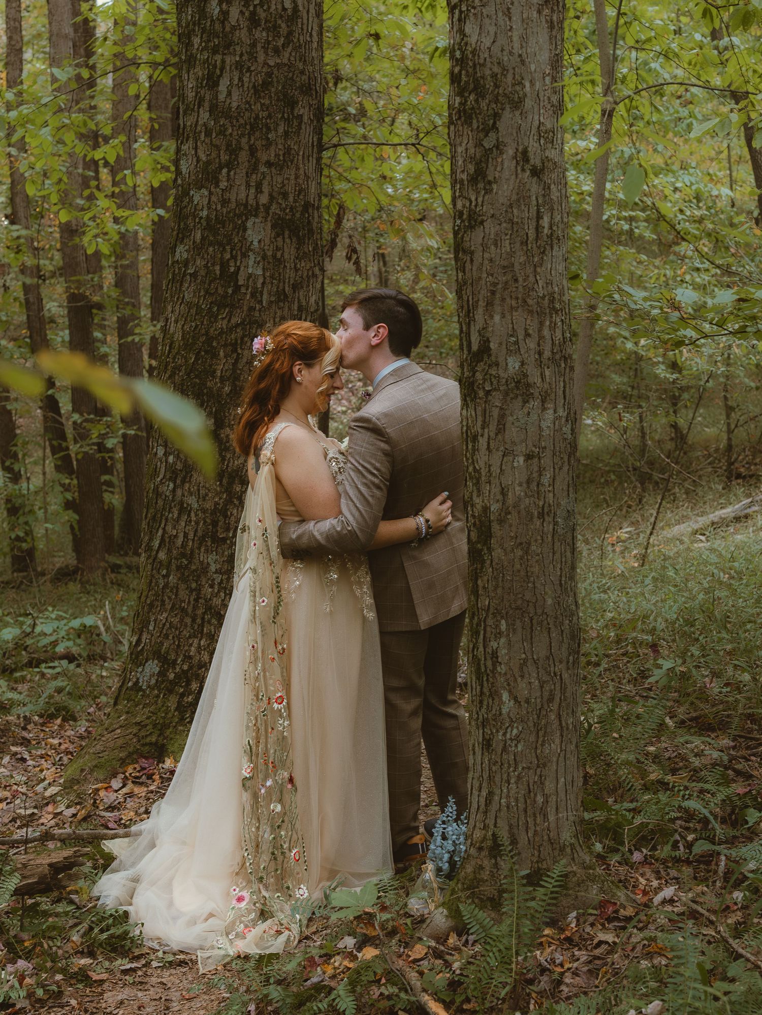 Romantic woodland wedding portrait of couple embracing between tall trees.