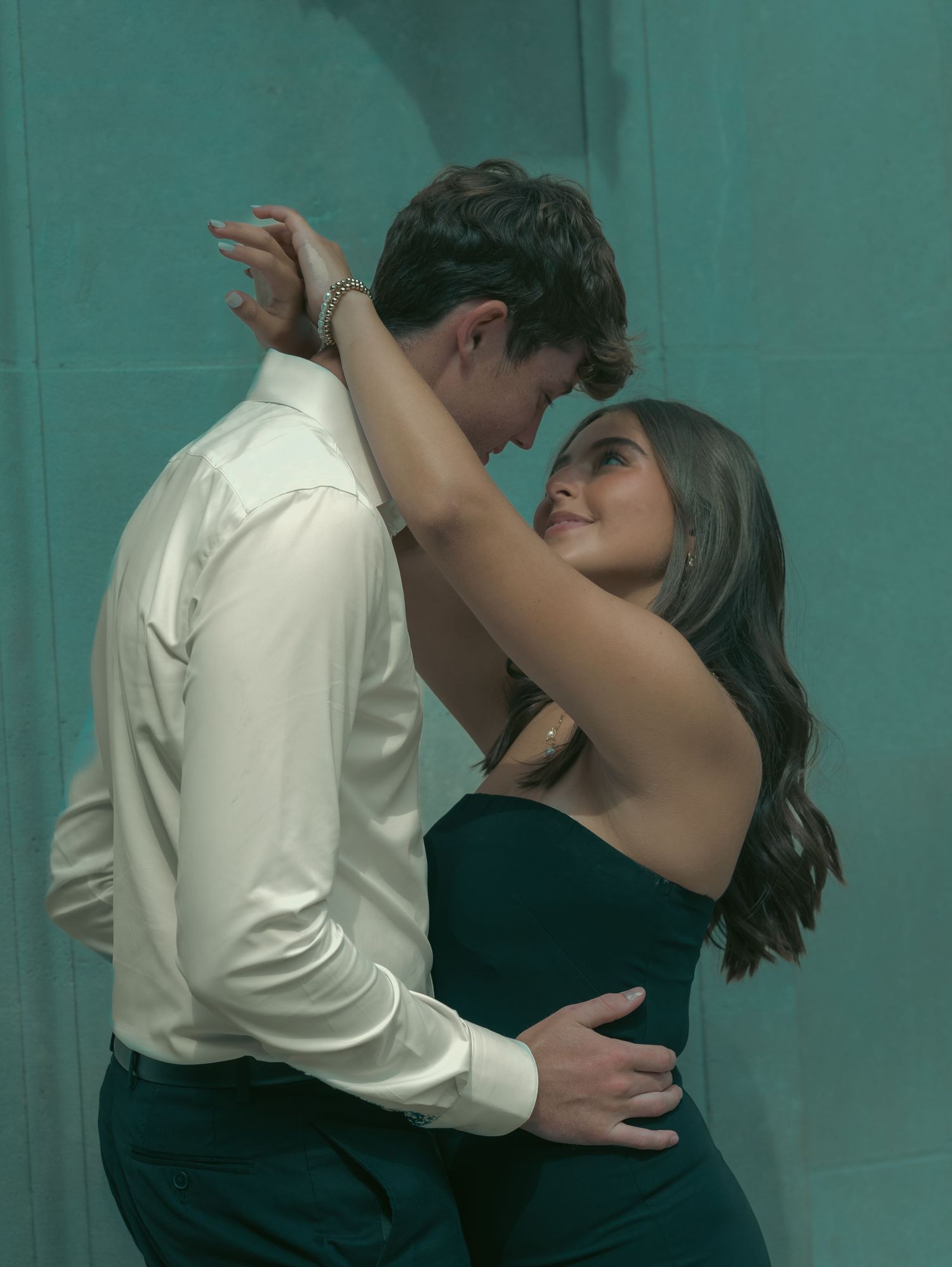 A couple sharing an intimate dance moment against a teal colored wall background.