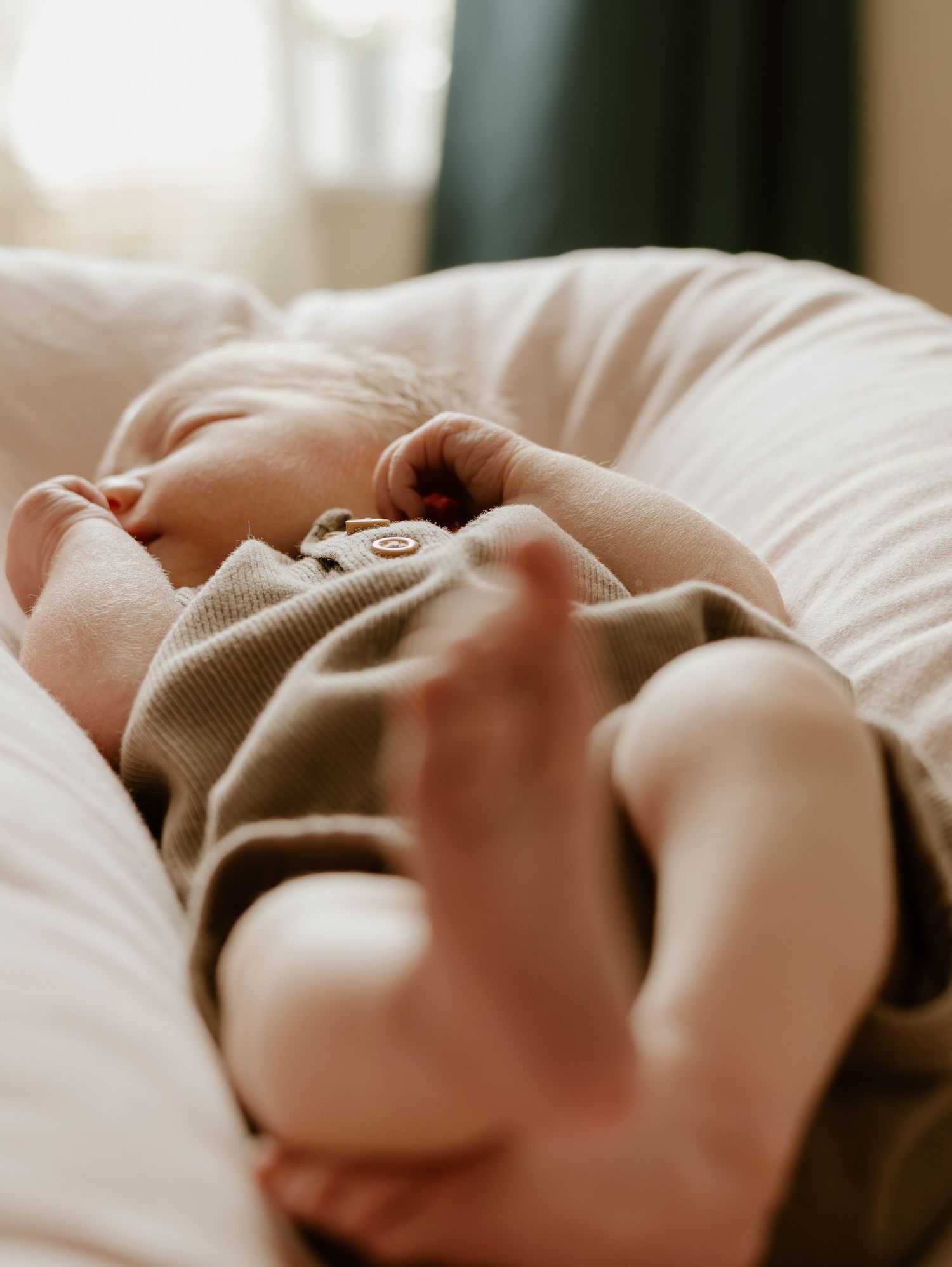 Sleeping baby wearing cozy beige sweater resting on white bedding.