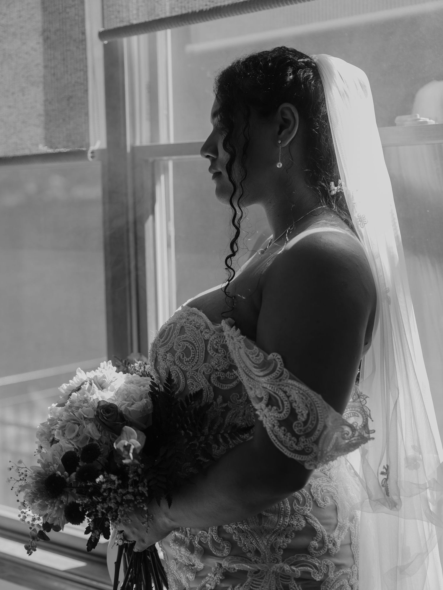 Elegant bridal silhouette by window holding classic white and pink bouquet.